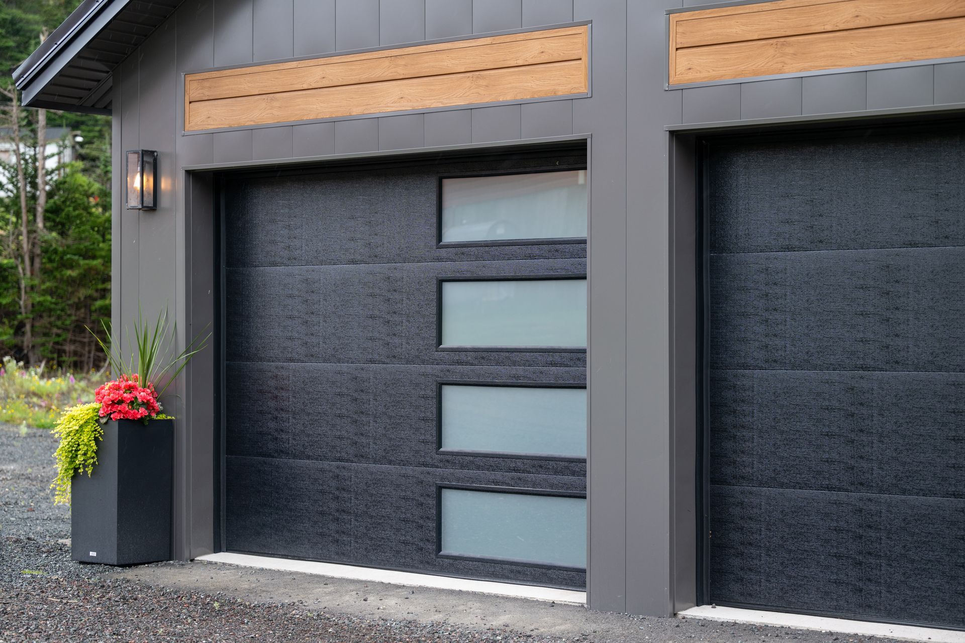 Two-car garage with dark gray doors and frosted glass windows, gray siding, and wooden accents.