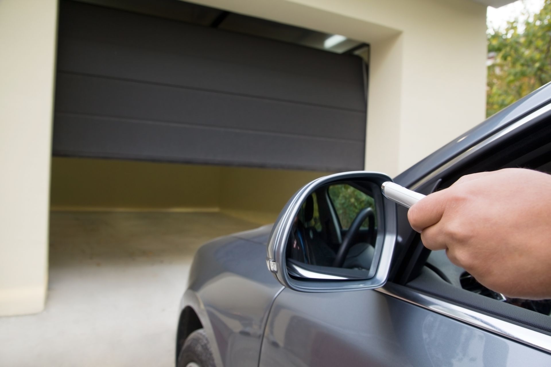 A person in a gray car activates the garage door opener. 
