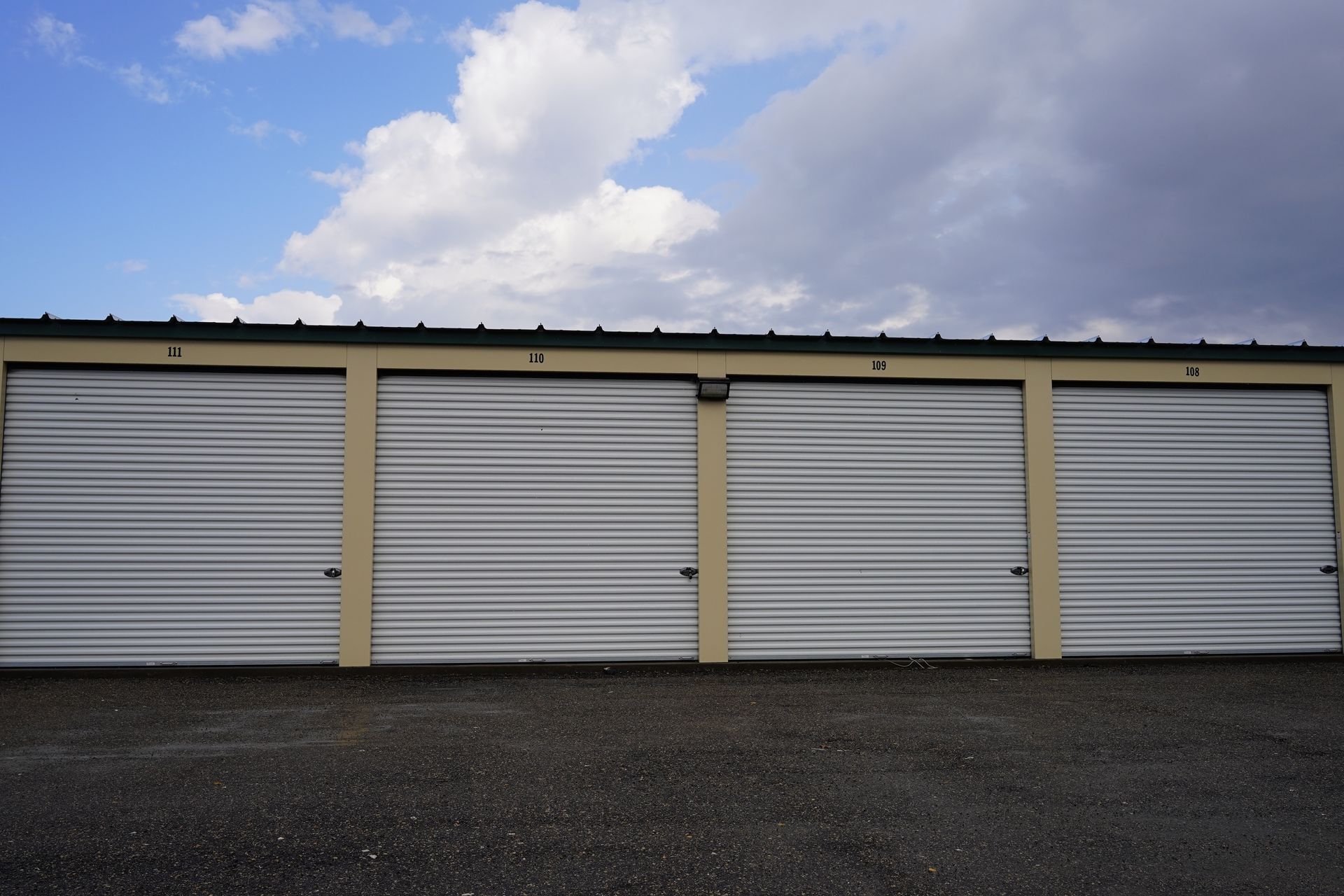 Four storage units with closed metal doors under a cloudy sky.