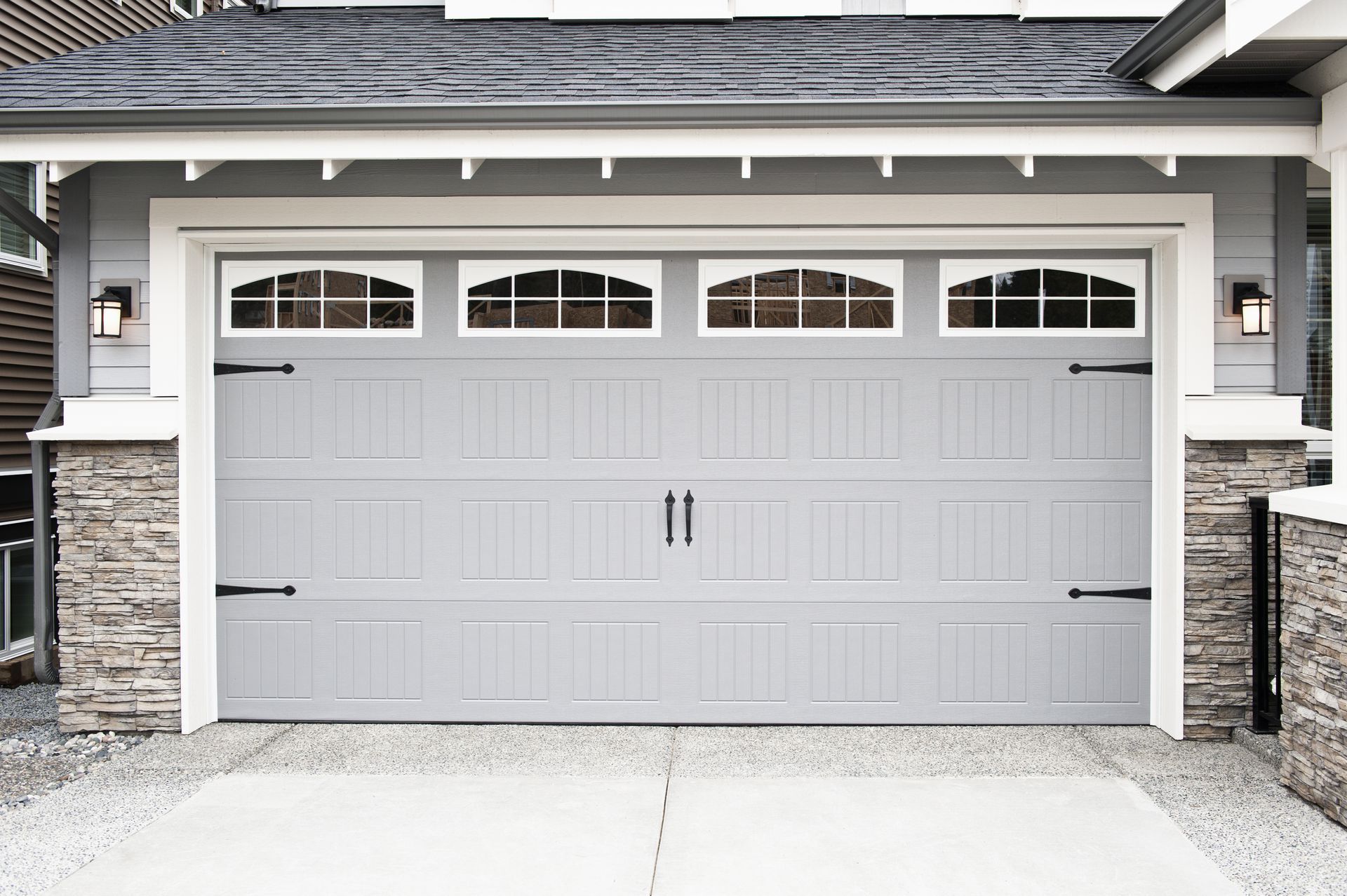 Gray garage door with arched windows, black hardware, and stone accents.