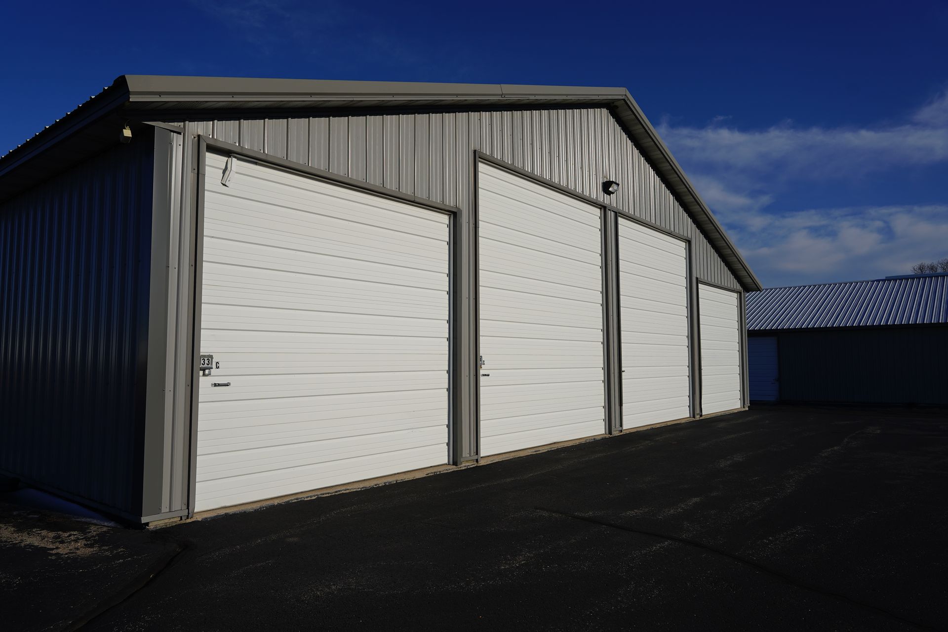 Metal storage building with three white garage doors and a dark asphalt surface.