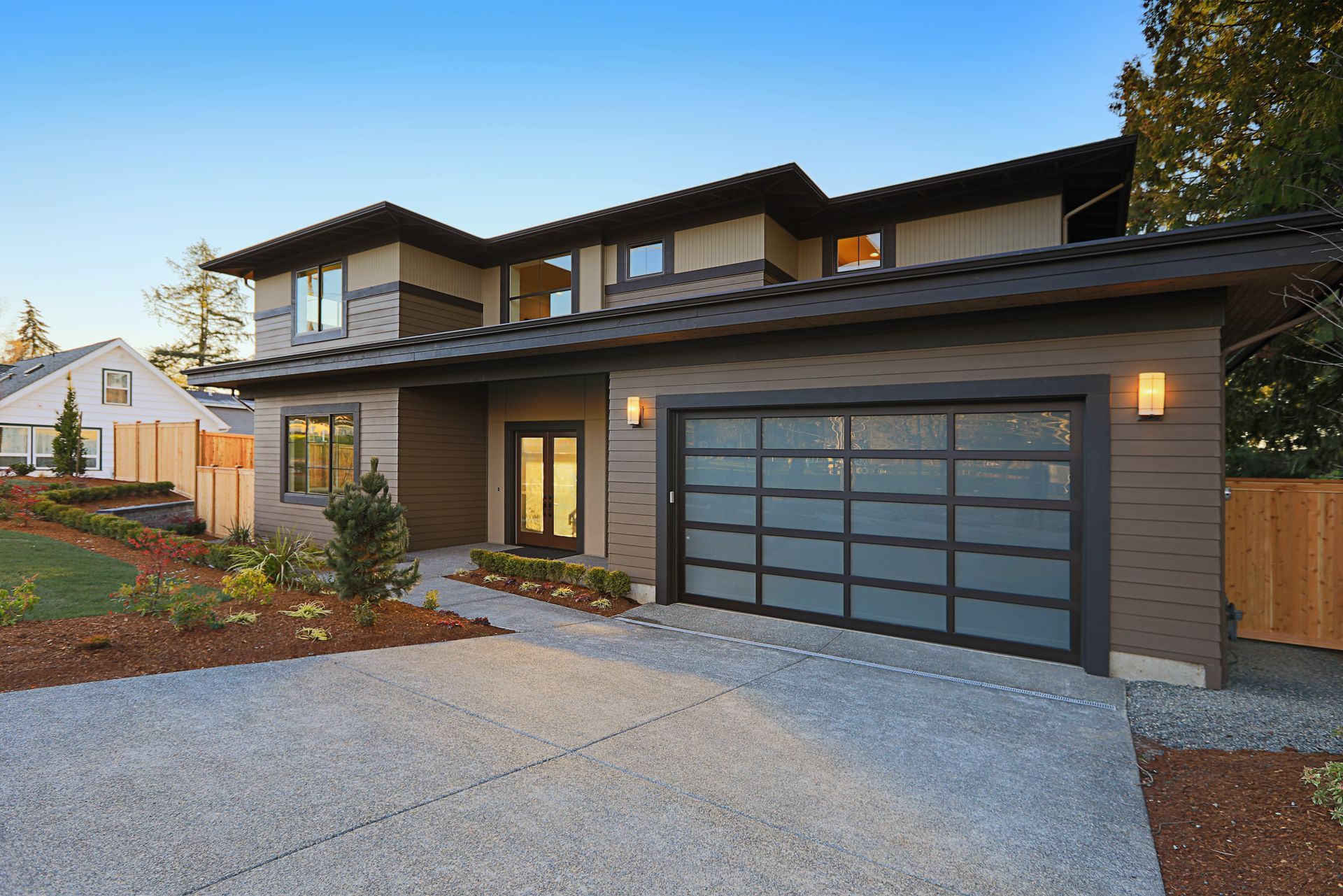 Modern house with a gray driveway, glass garage door, and brown siding.