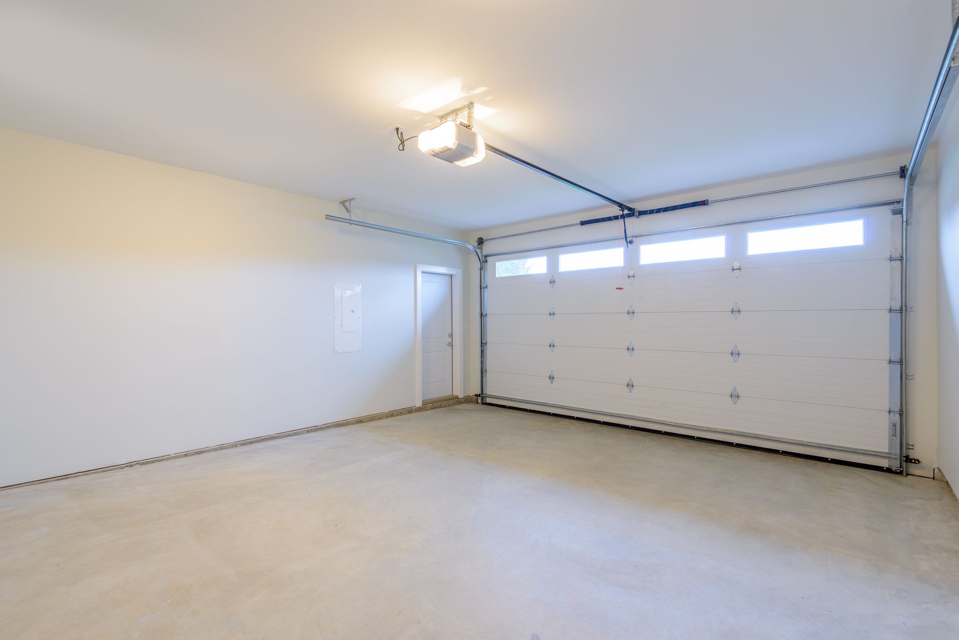 Empty garage interior with white walls, concrete floor, and overhead garage door.
