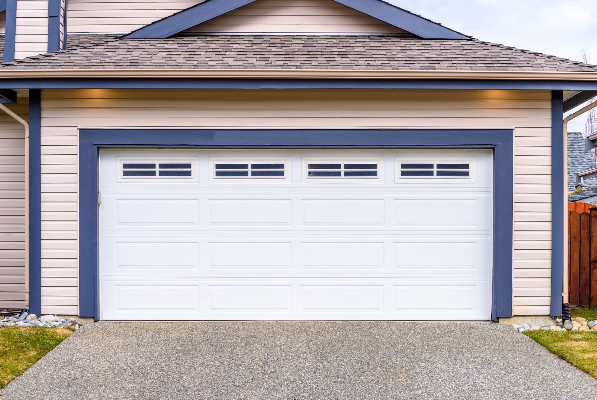 White garage door with blue trim on a tan house with a gravel driveway.