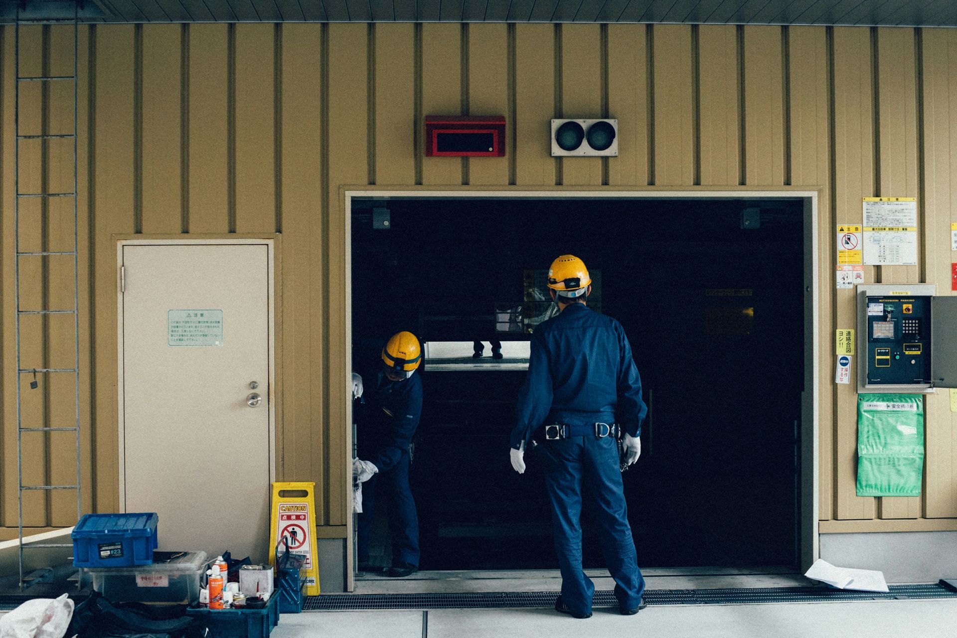 Two workers in blue uniforms and yellow helmets inside a loading dock entrance.