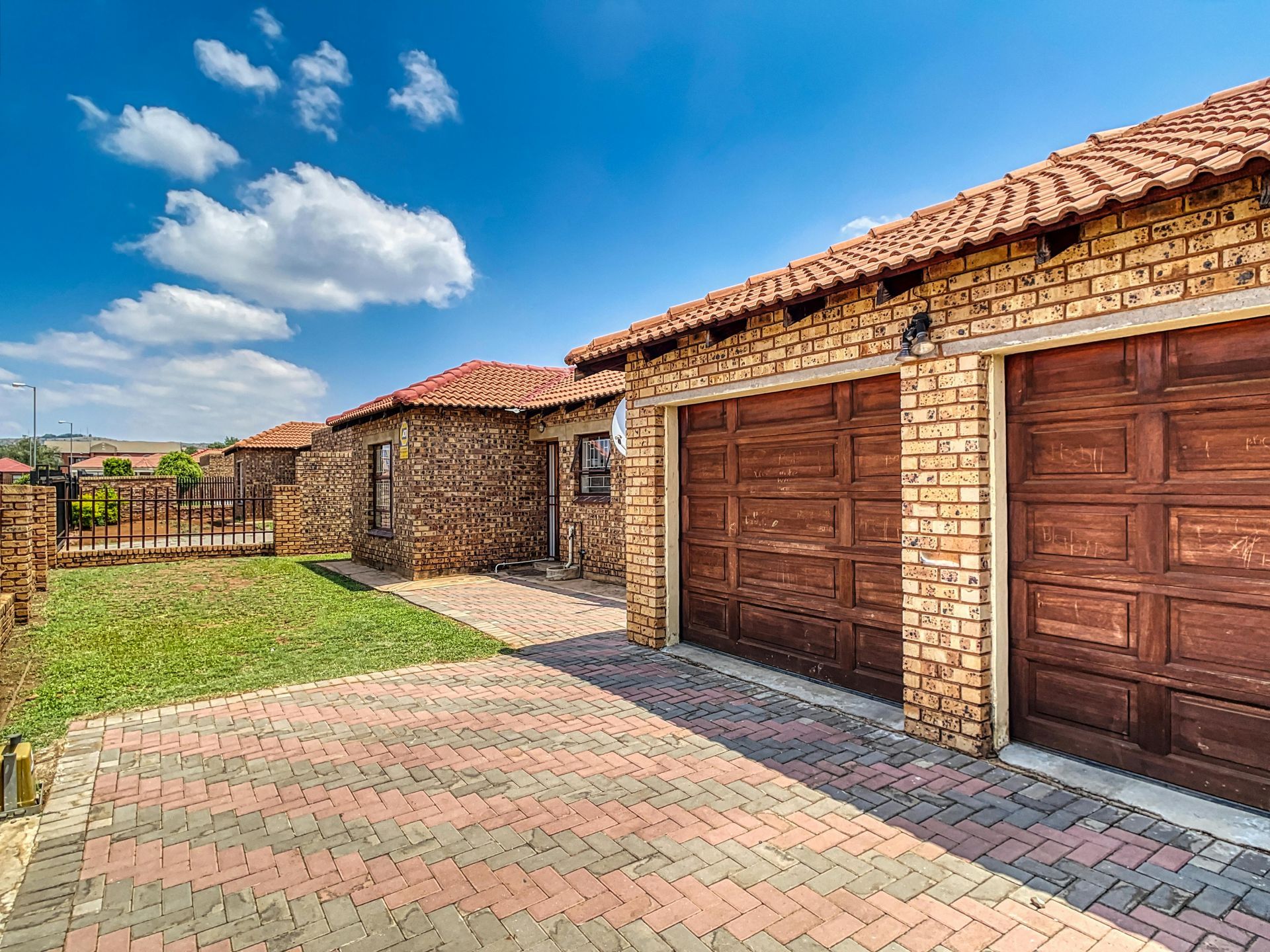 Brick houses with brown garage doors and red tile roofs against a blue sky.