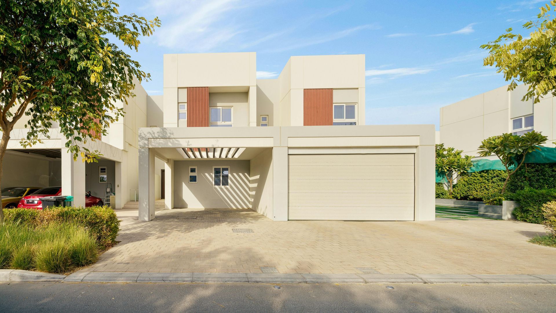Modern two-story house with garage and carports; beige exterior, trees, and blue sky.