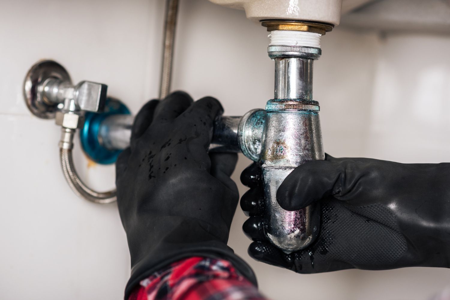 Hands in black gloves tighten a chrome pipe under a sink.