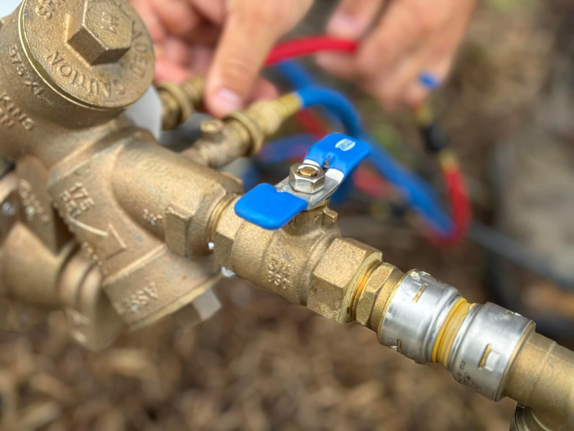 A person's hand near brass water valve, with blue handle, connected to pipes.