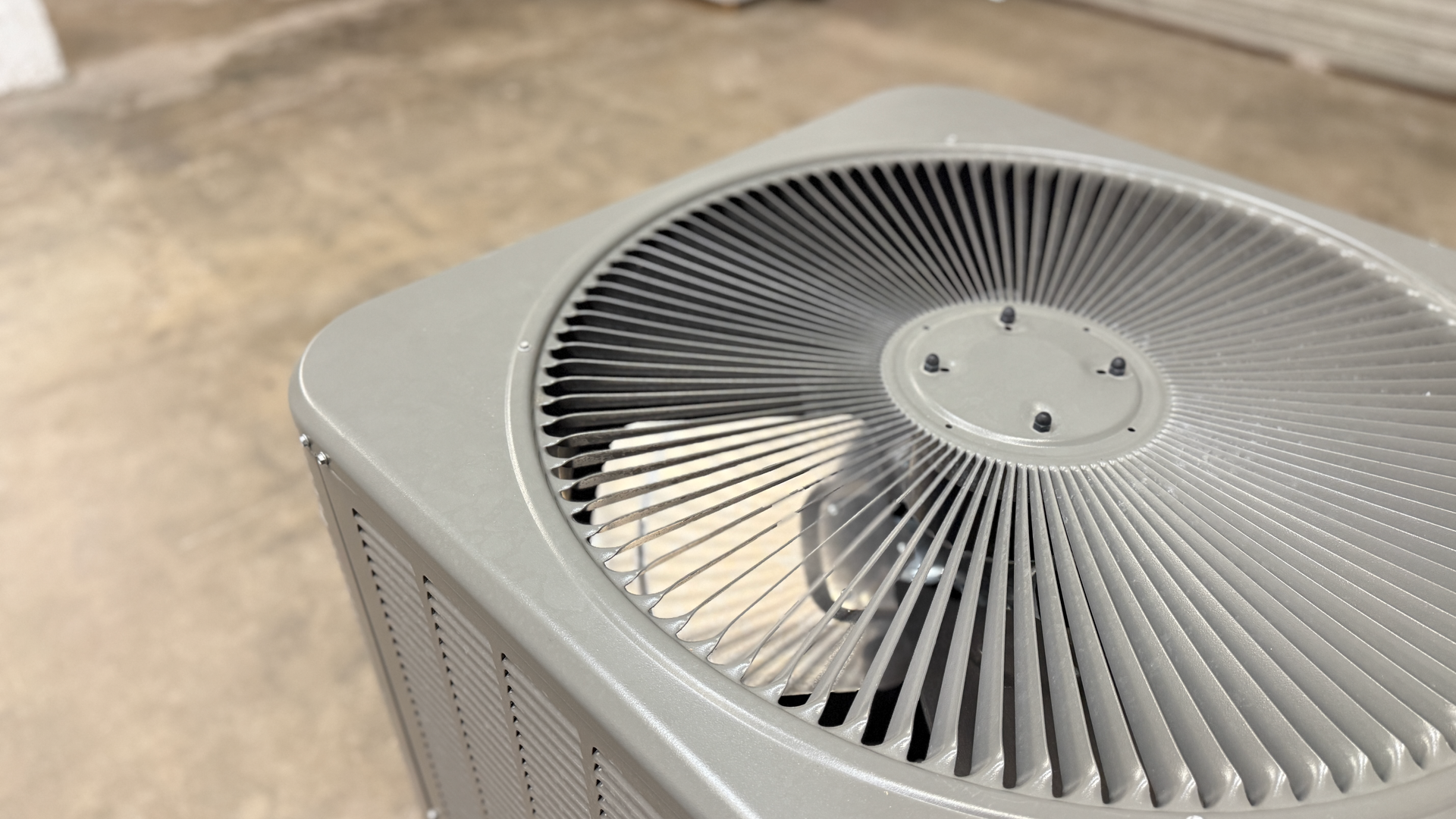 Gray air conditioning unit with fan blades against a cement floor.