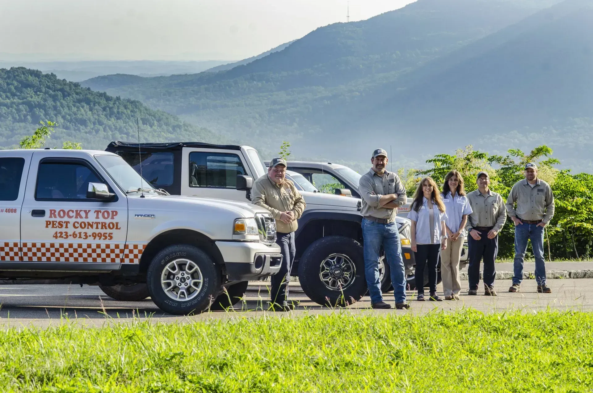 People standing by trucks in front of mountains;