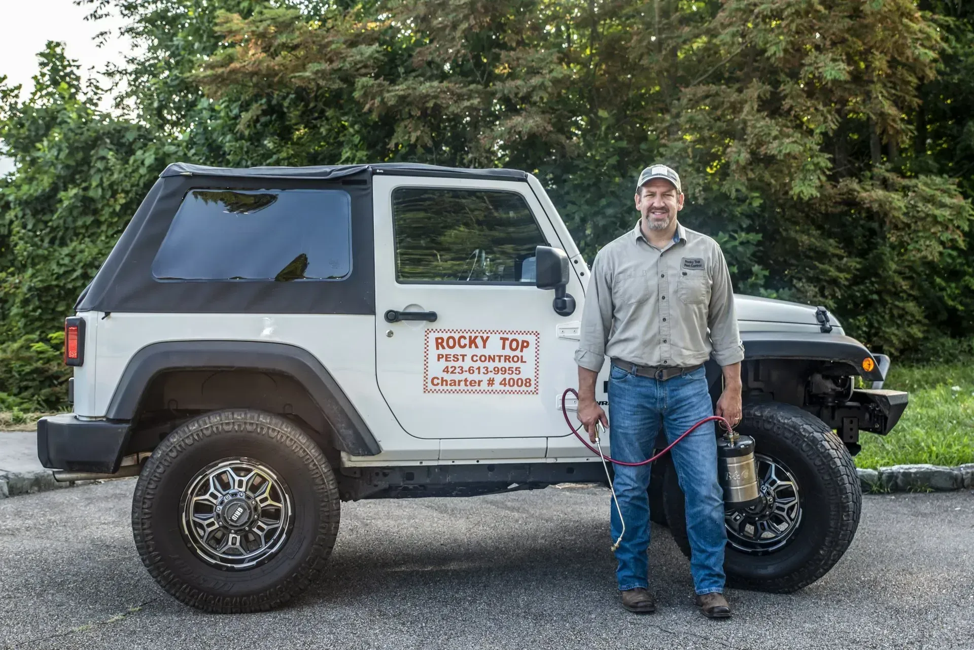 Man stands beside a white Jeep. He holds a hose, likely for pest control. The Jeep has a business logo.