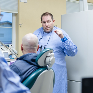 Dentist examining a child's teeth in a dental chair. The dentist wears a mask and gloves.