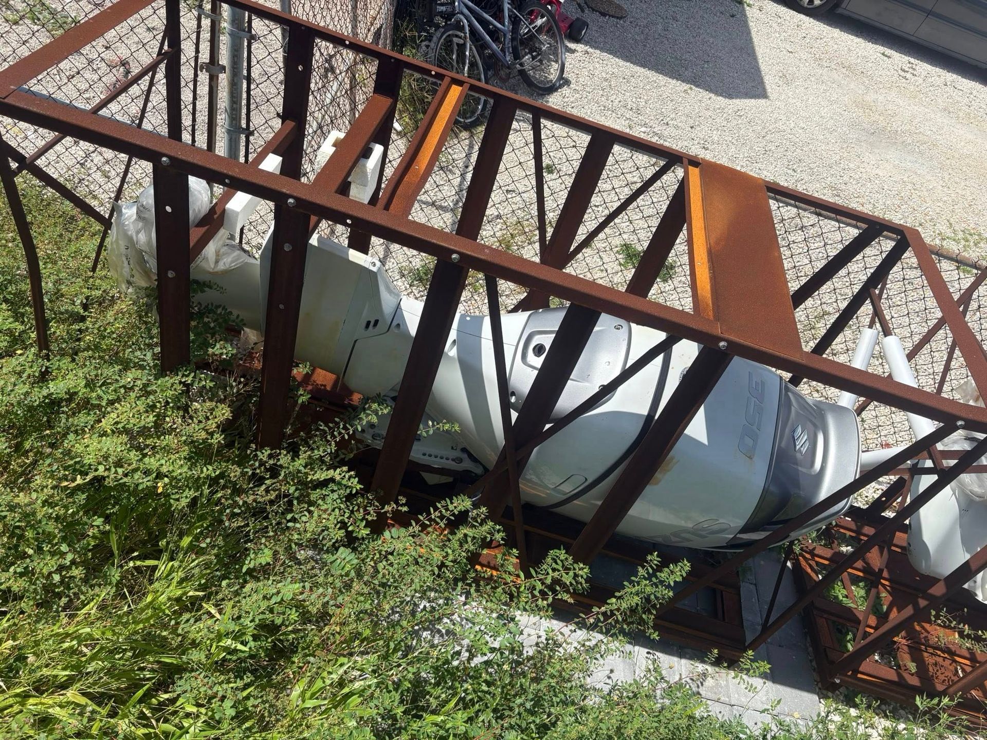 White car wedged under a rusted metal fence beside a road and greenery