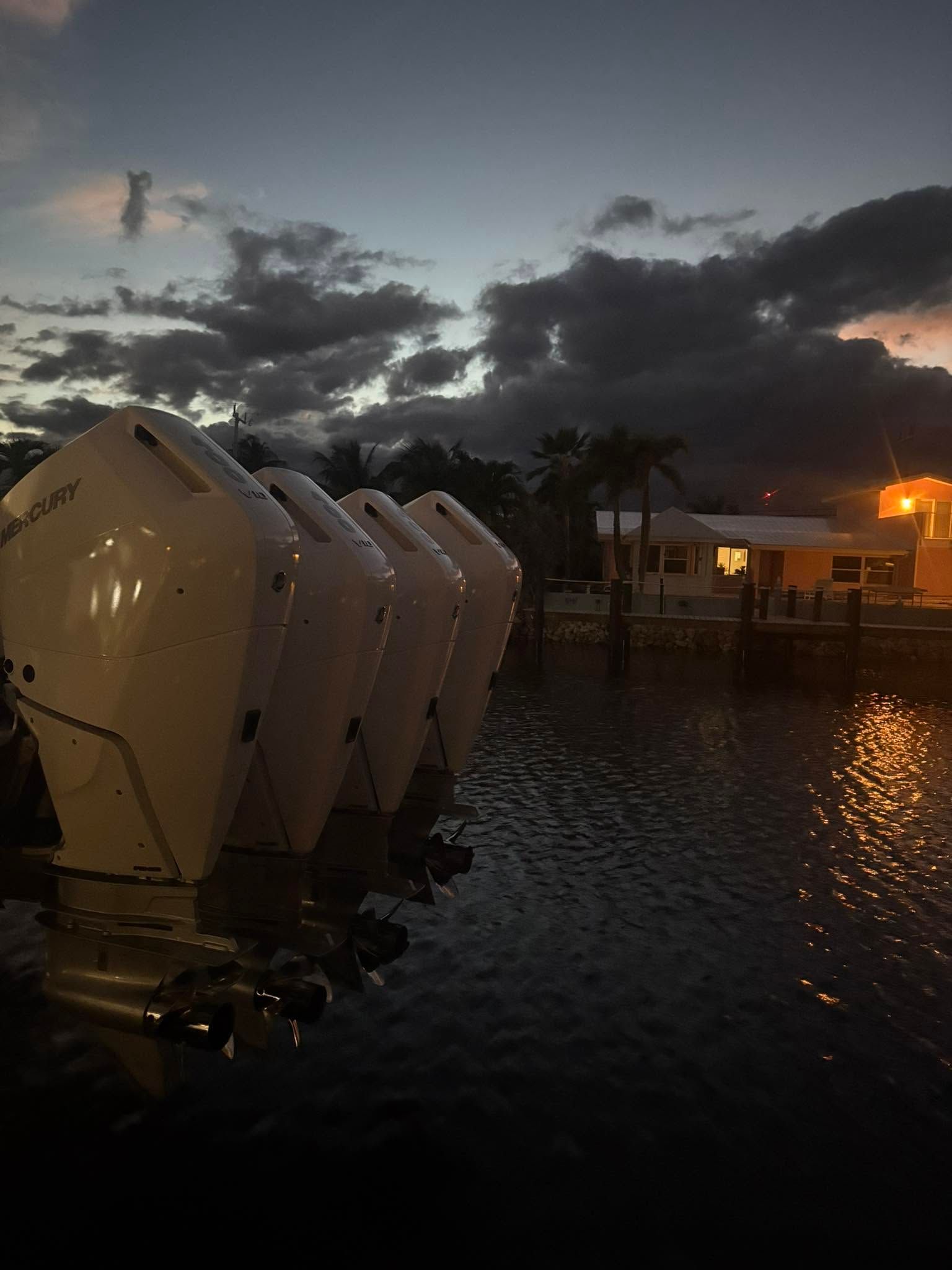 Dusk over a marina with rows of white boats on calm water and an orange-lit dock under cloudy skies