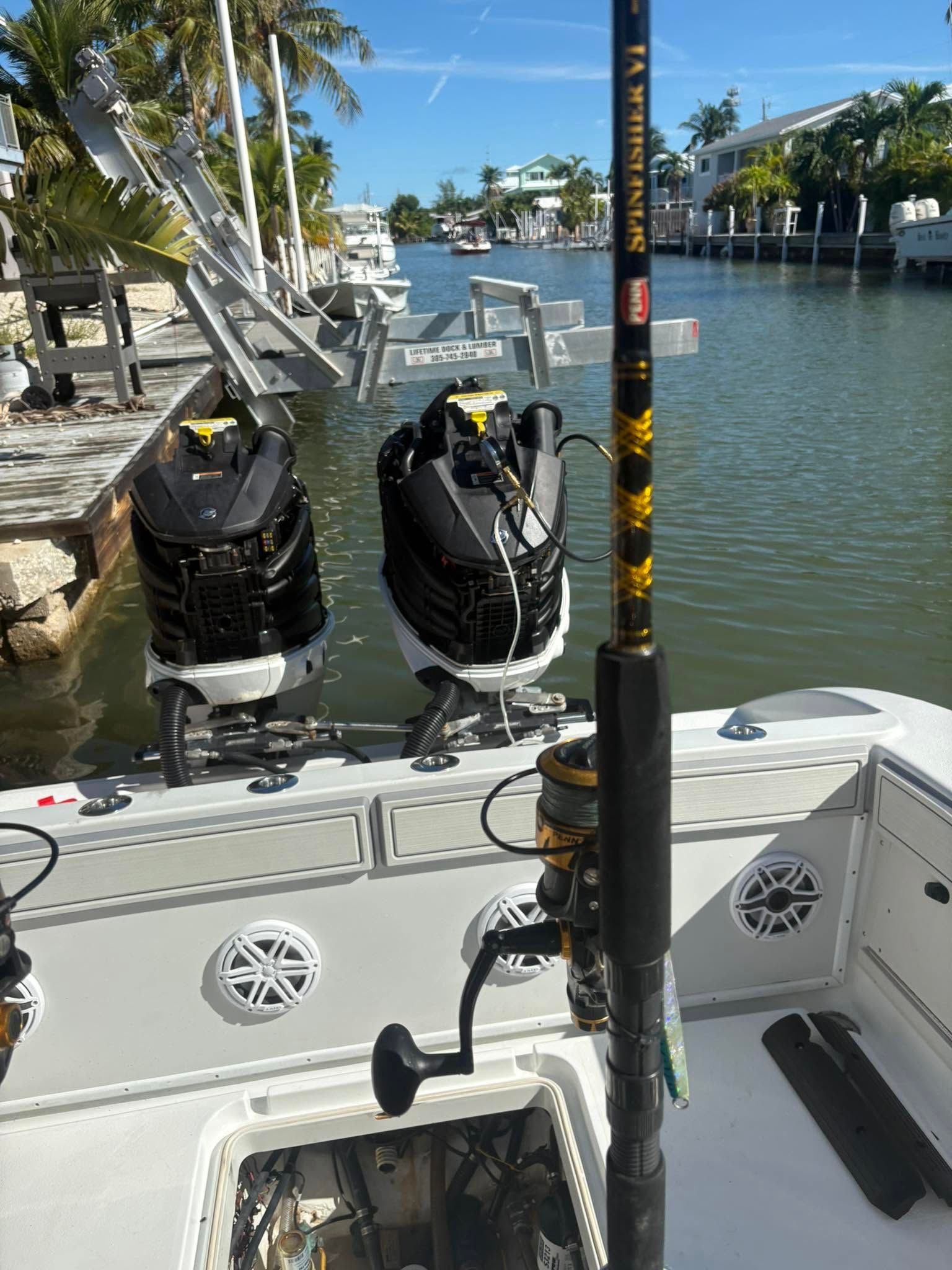 Boat stern with twin outboard motors, fishing rod, and sunny canal view under a bridge