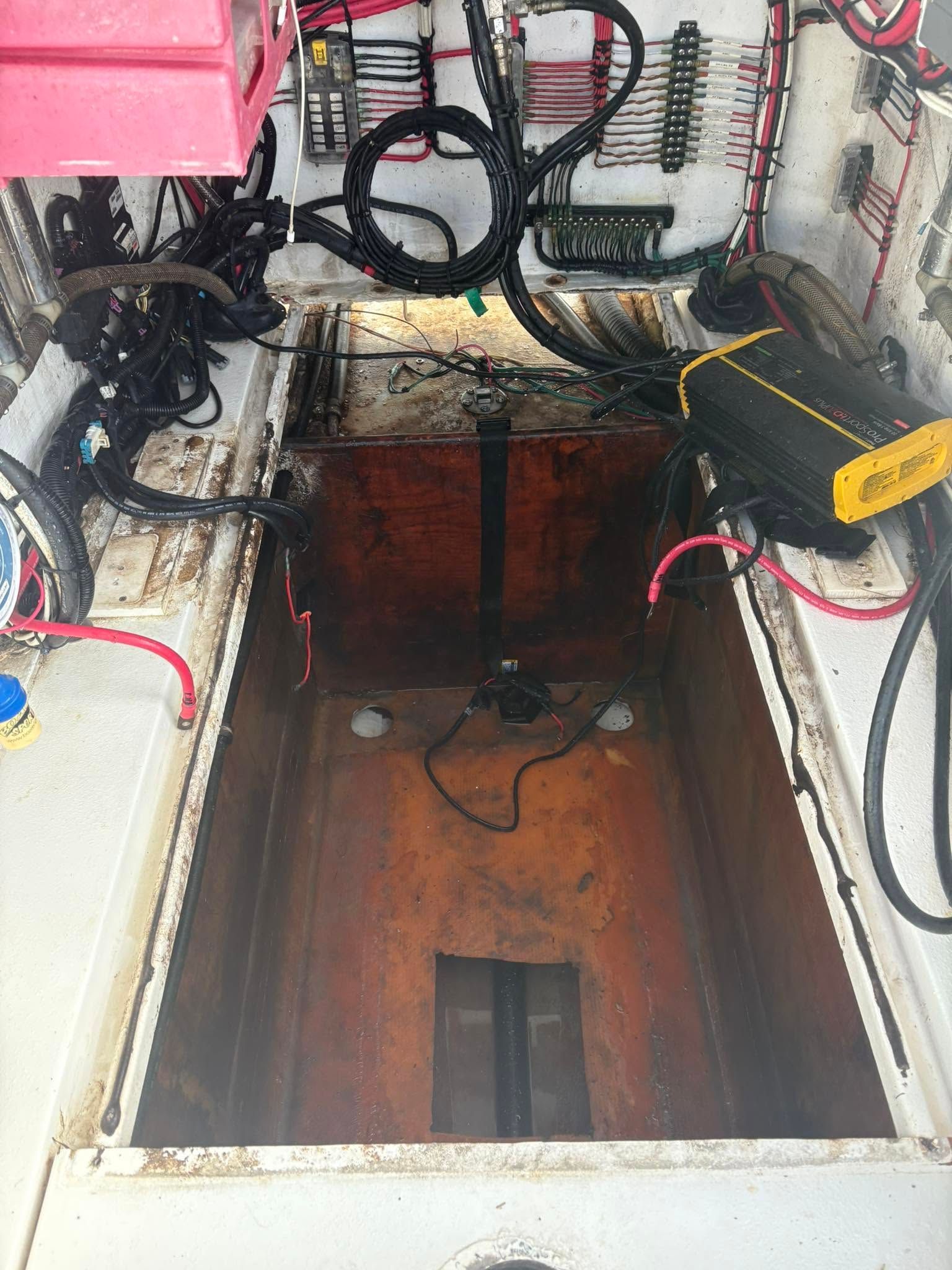 Open hatch on a boat deck, revealing a narrow rust-colored compartment with cables and machinery.