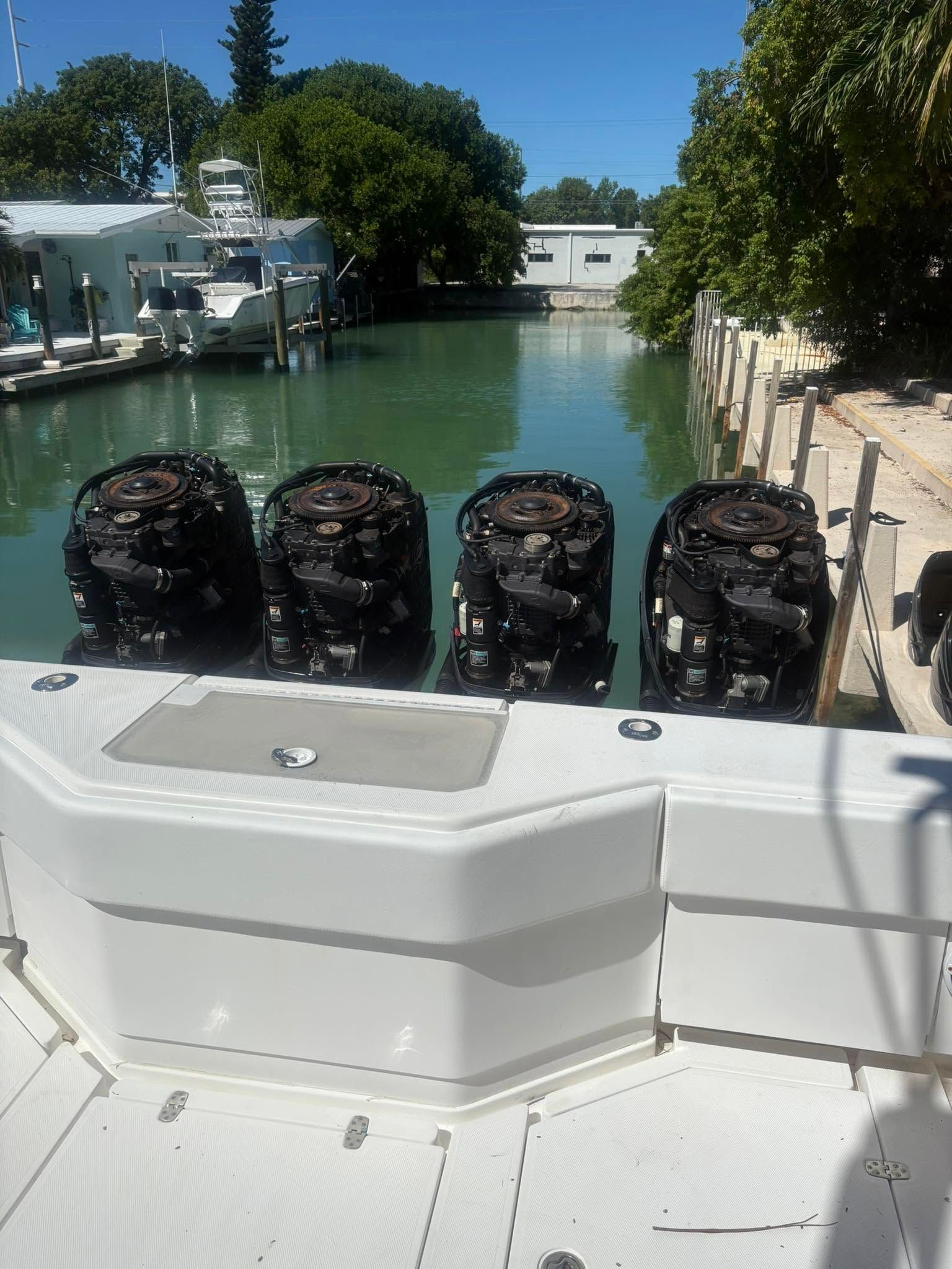 Boat stern with four black outboard motors docked in a marina canal on a sunny day