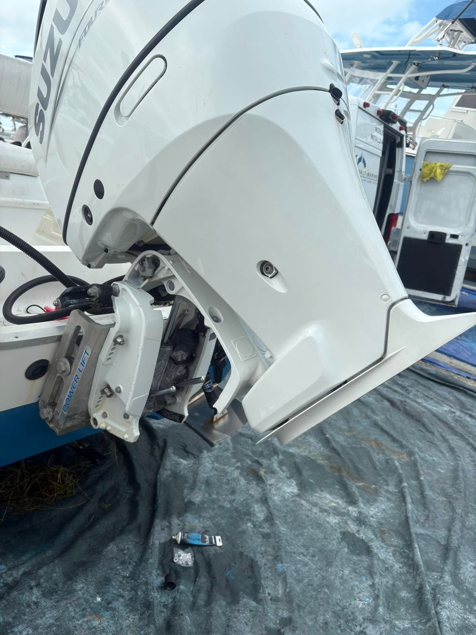 Damaged white boat engine mounted on a vessel, with debris on the tarp-covered deck.
