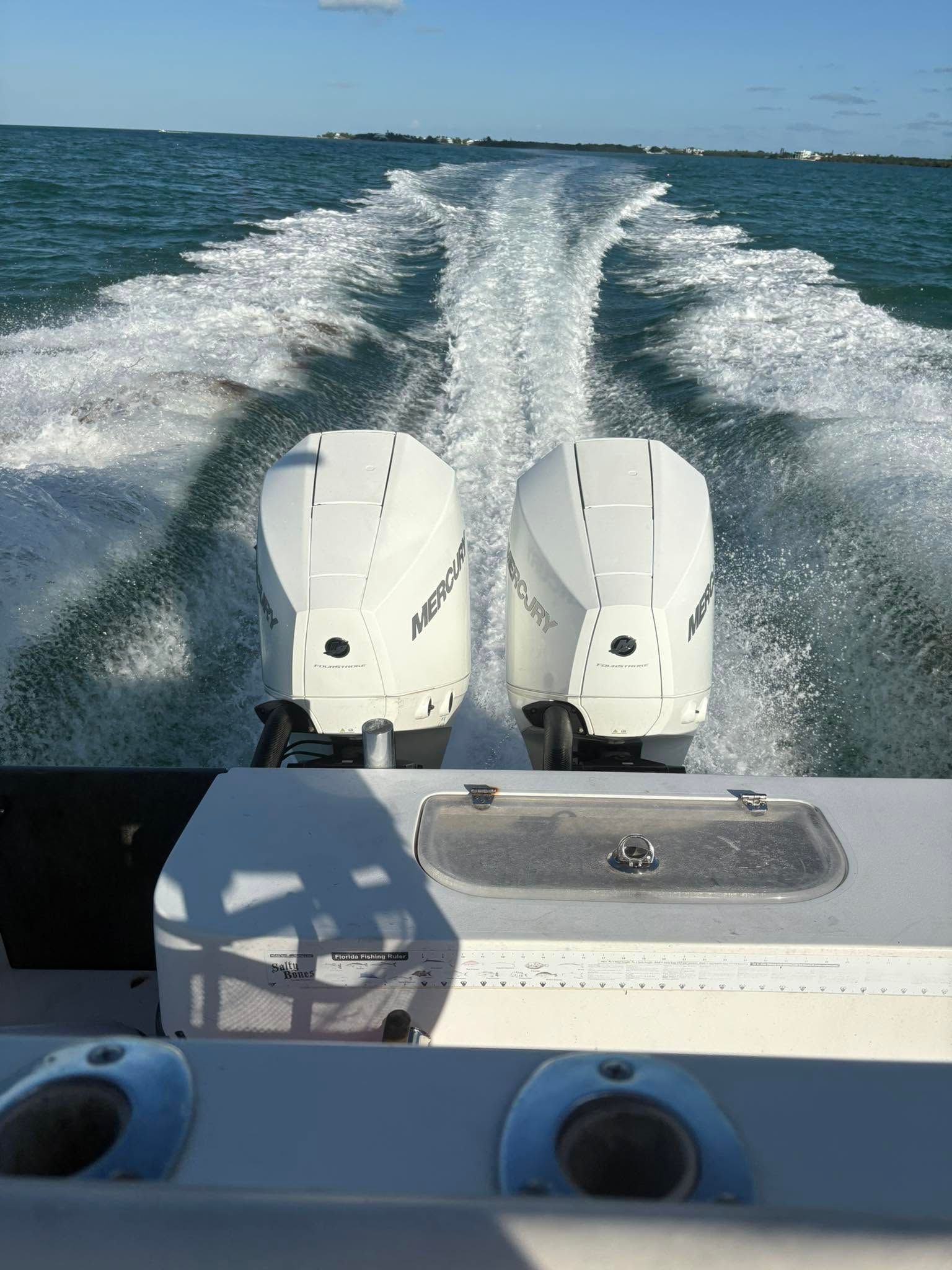 View from a boat stern, twin outboard motors cutting through blue water and leaving a foamy wake