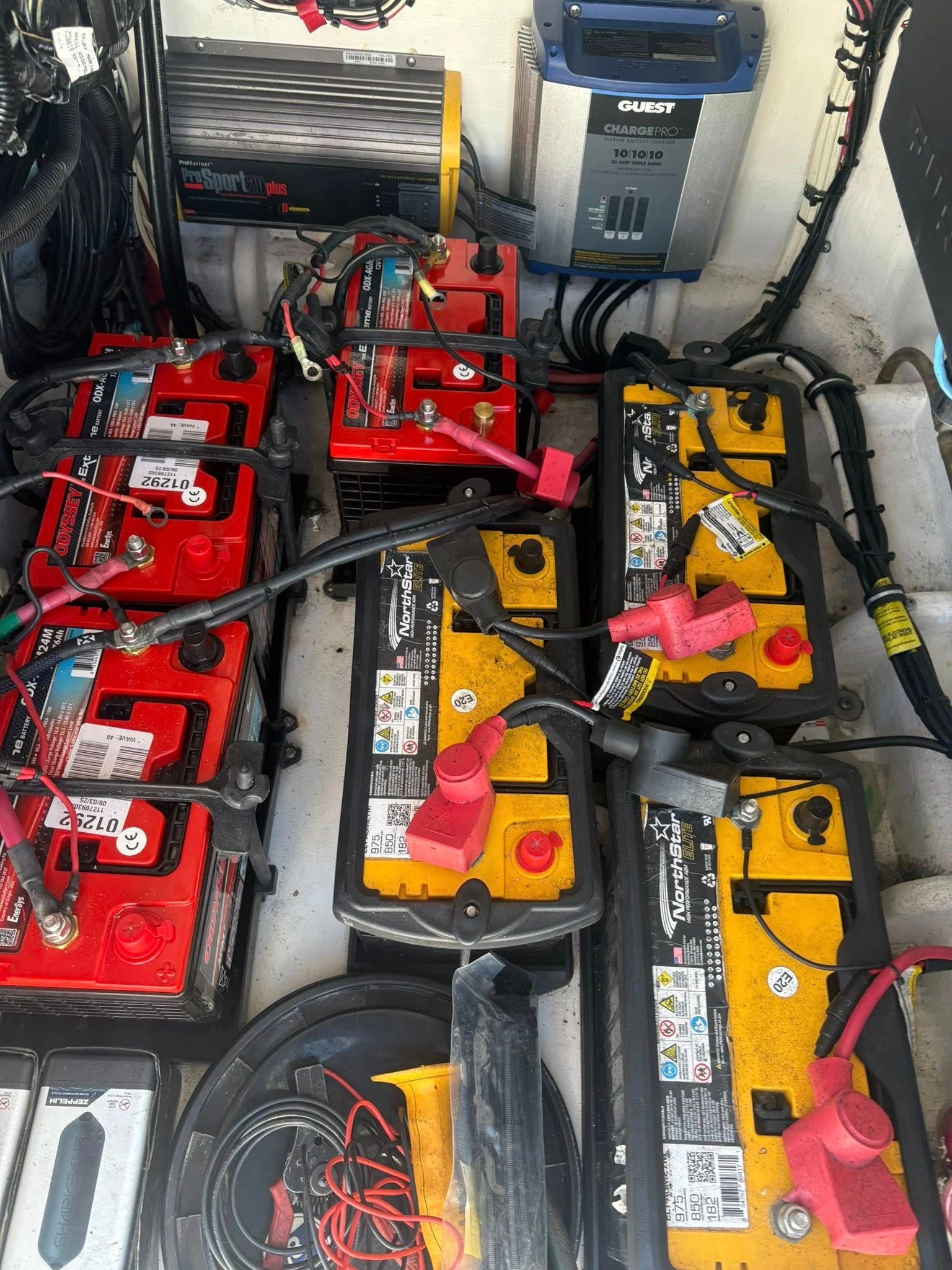 Battery bank with red and yellow batteries and wiring in a cramped compartment