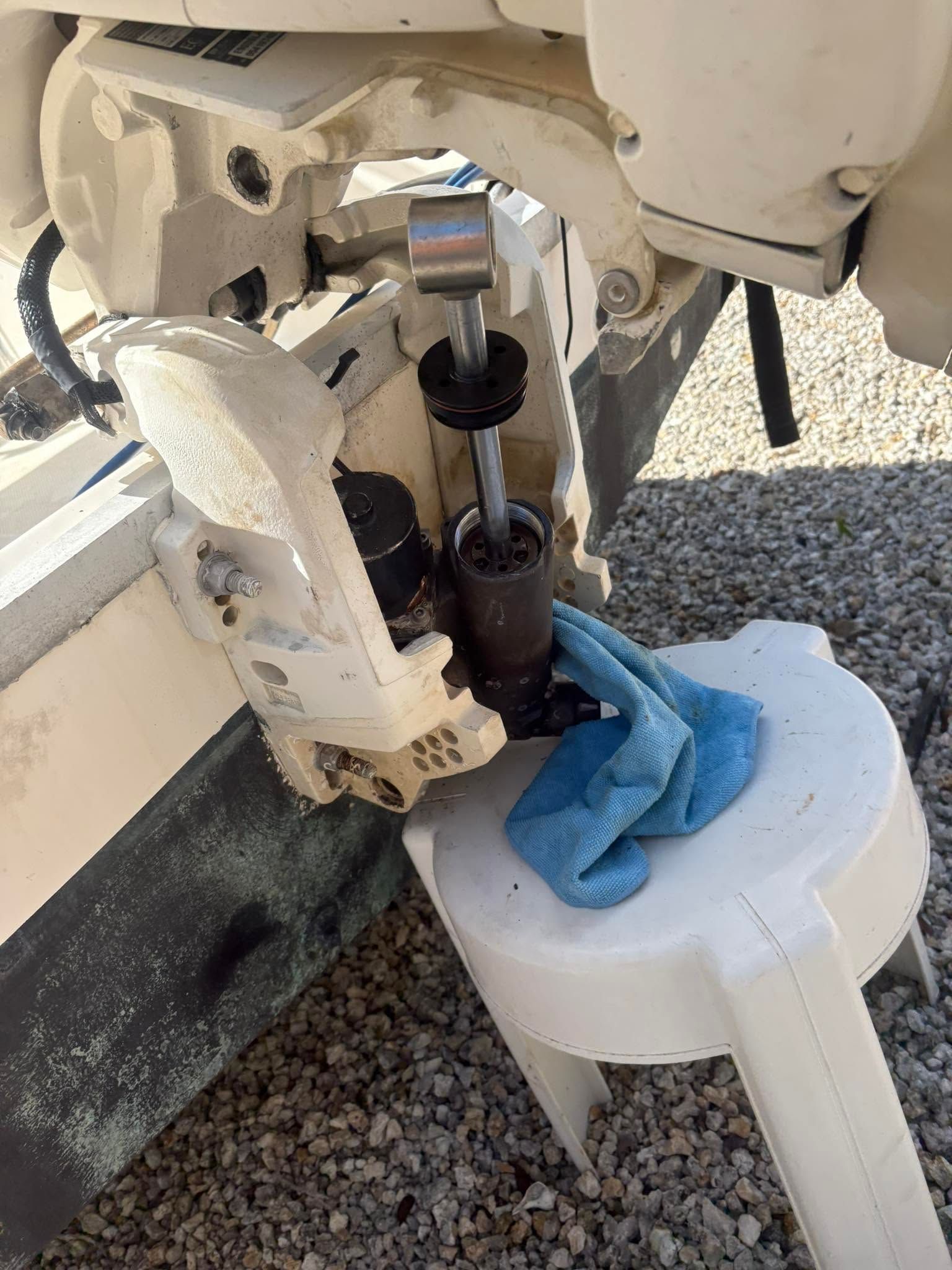 Close-up of a boat engine with a blue rag draped over a white container on gravel.