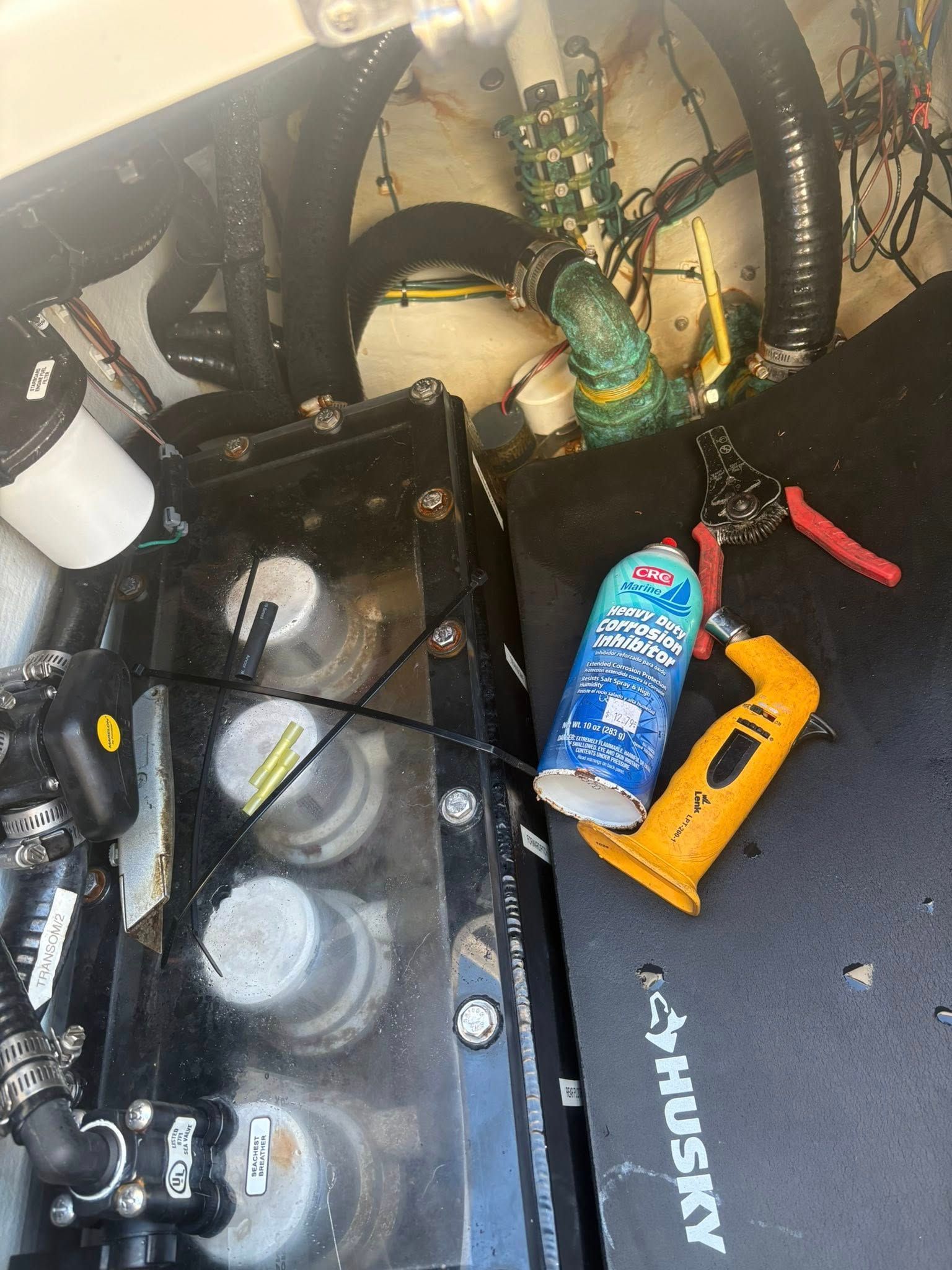 Cluttered car trunk with battery, cleaning spray can, yellow tool, and hoses or cables.