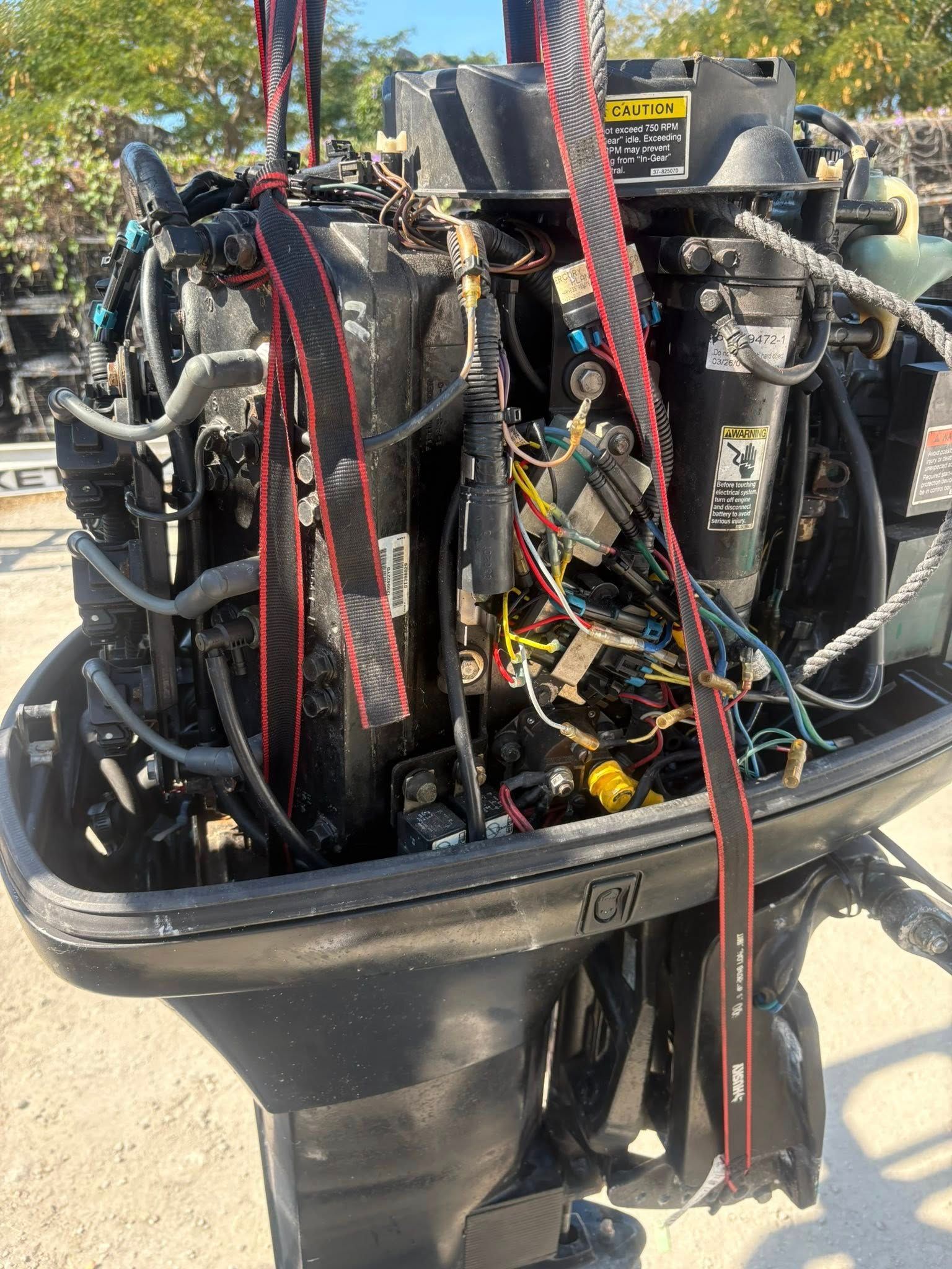 Close-up of a boat engine with exposed wiring and red straps on a dockside surface.