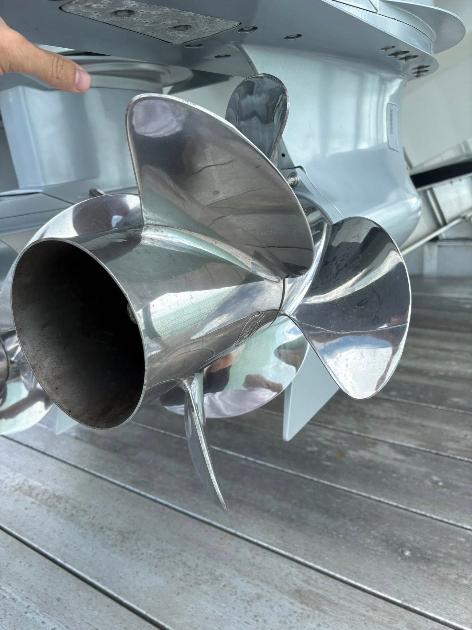 Shiny metal propeller on a boat deck, with a hand holding it in place.