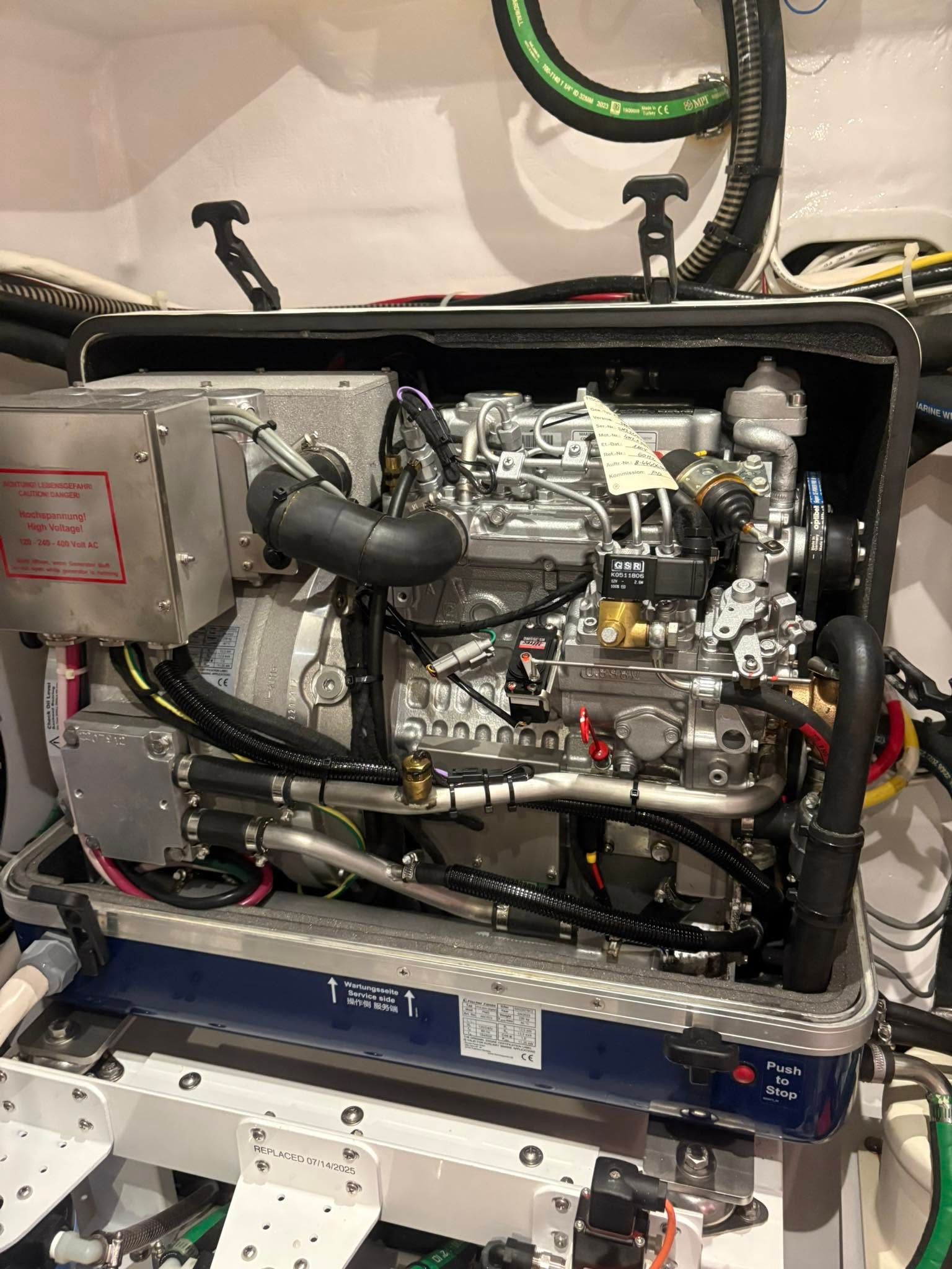 Open engine compartment with exposed machinery, hoses, and wiring in a white vehicle or machine bay