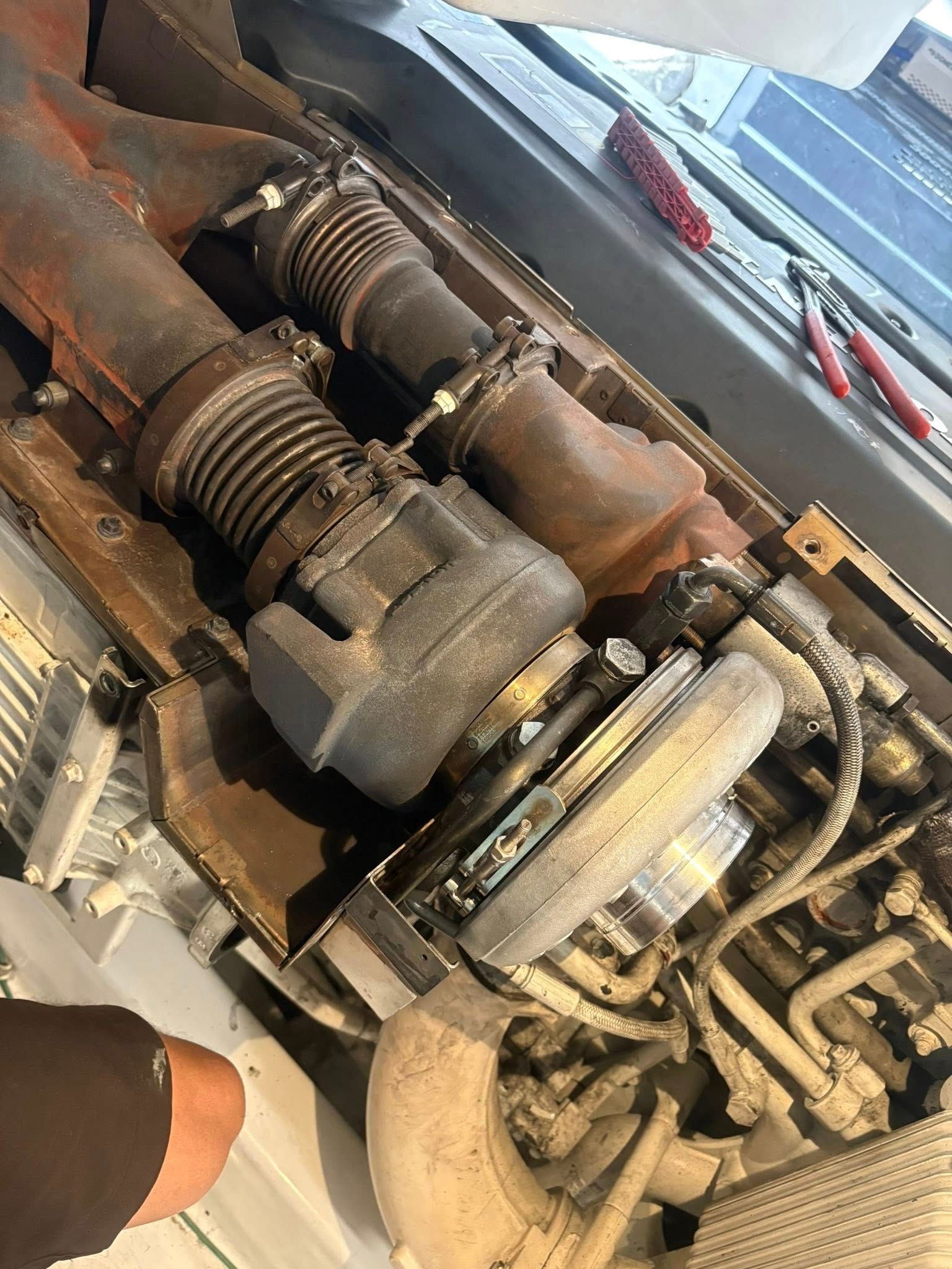 Close-up of a damaged car engine with bent hoses and corroded metal parts on a workbench