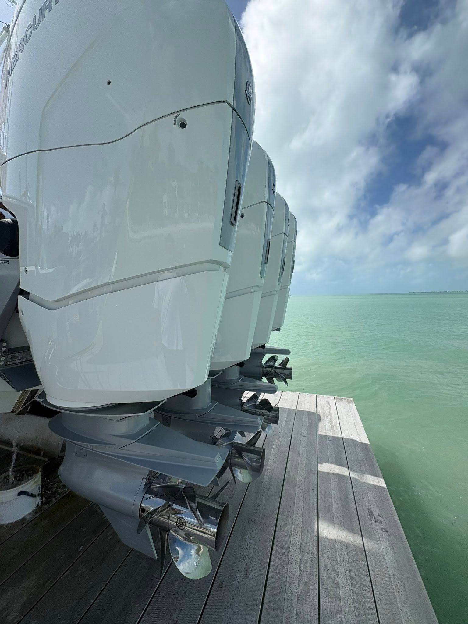 Close-up of white wind turbine blades beside a boardwalk over calm green water under cloudy sky