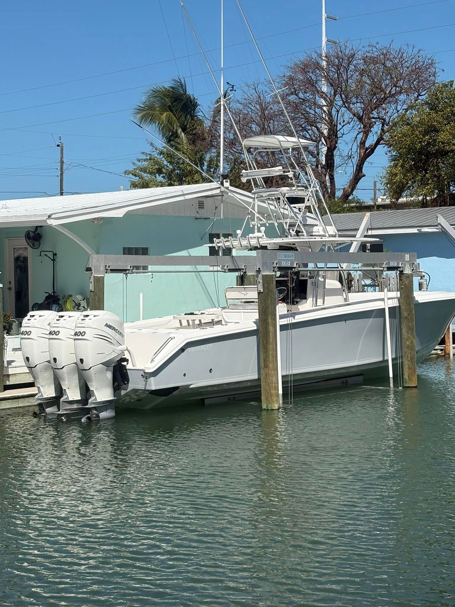 White fishing boat docked on calm water beside a house under a clear blue sky