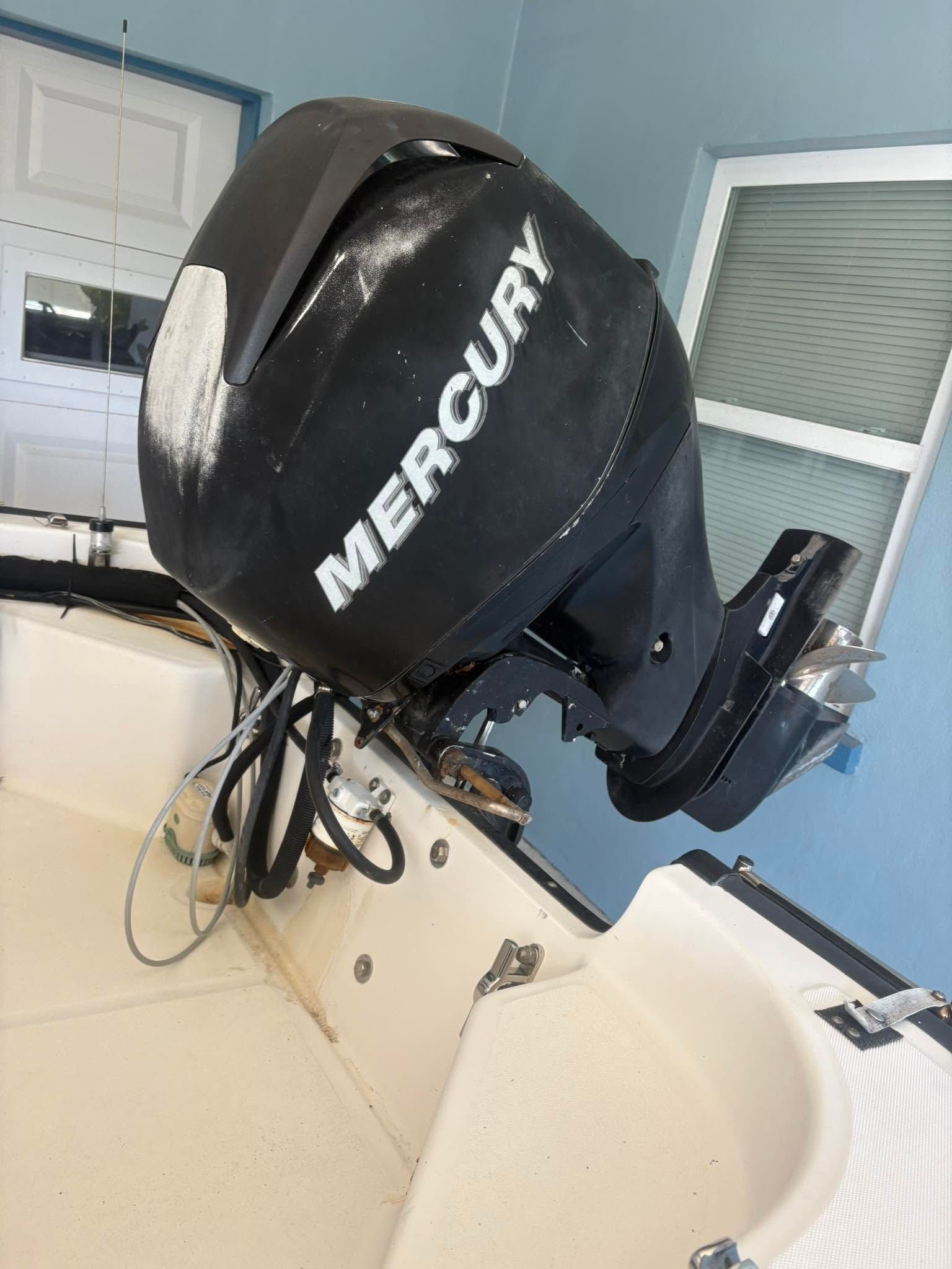 Black Mercury outboard motor mounted on a boat in a garage or workshop, beside a white seat.