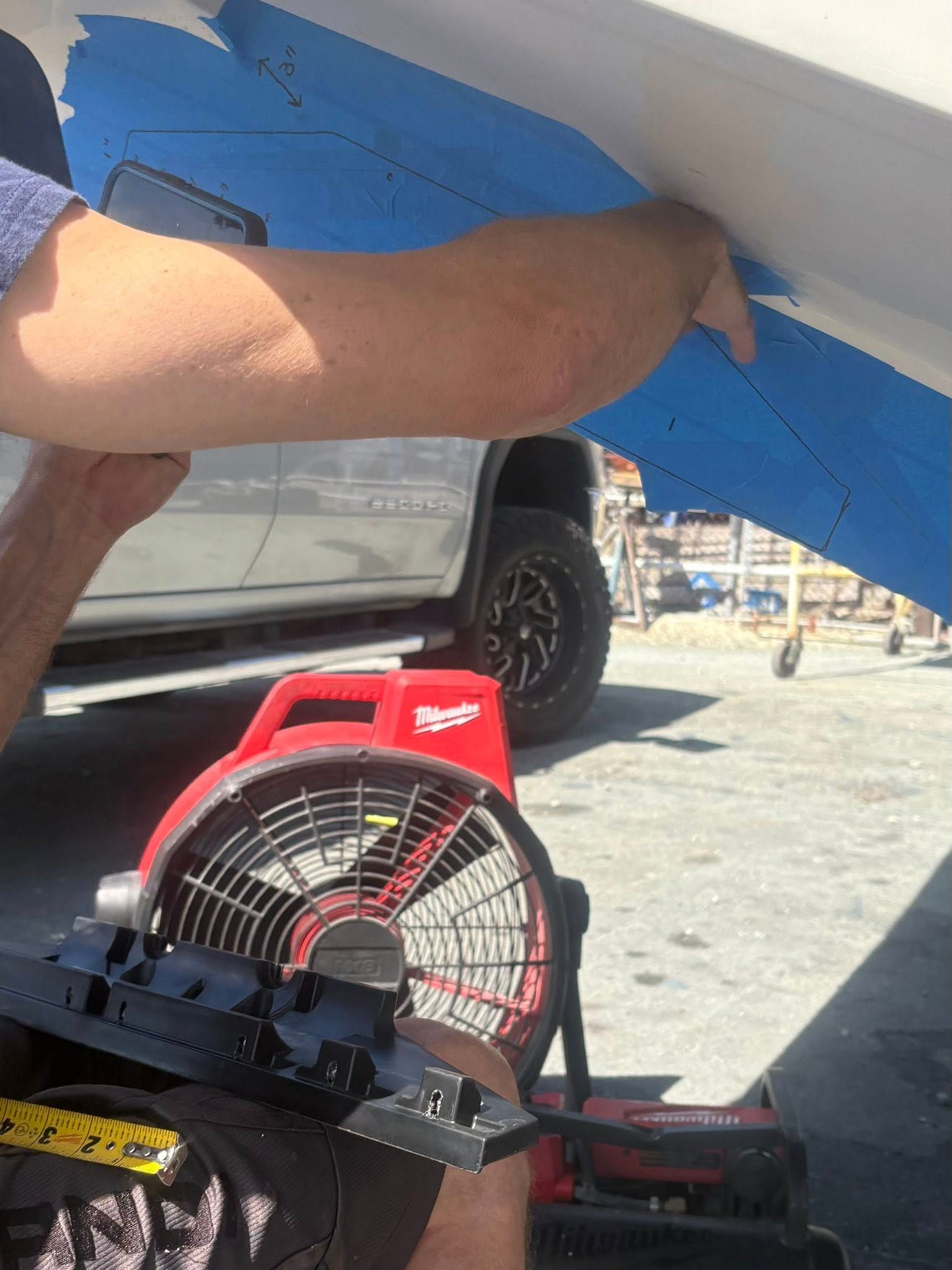 Person working on a blue vehicle with a red fan underneath in a garage or driveway