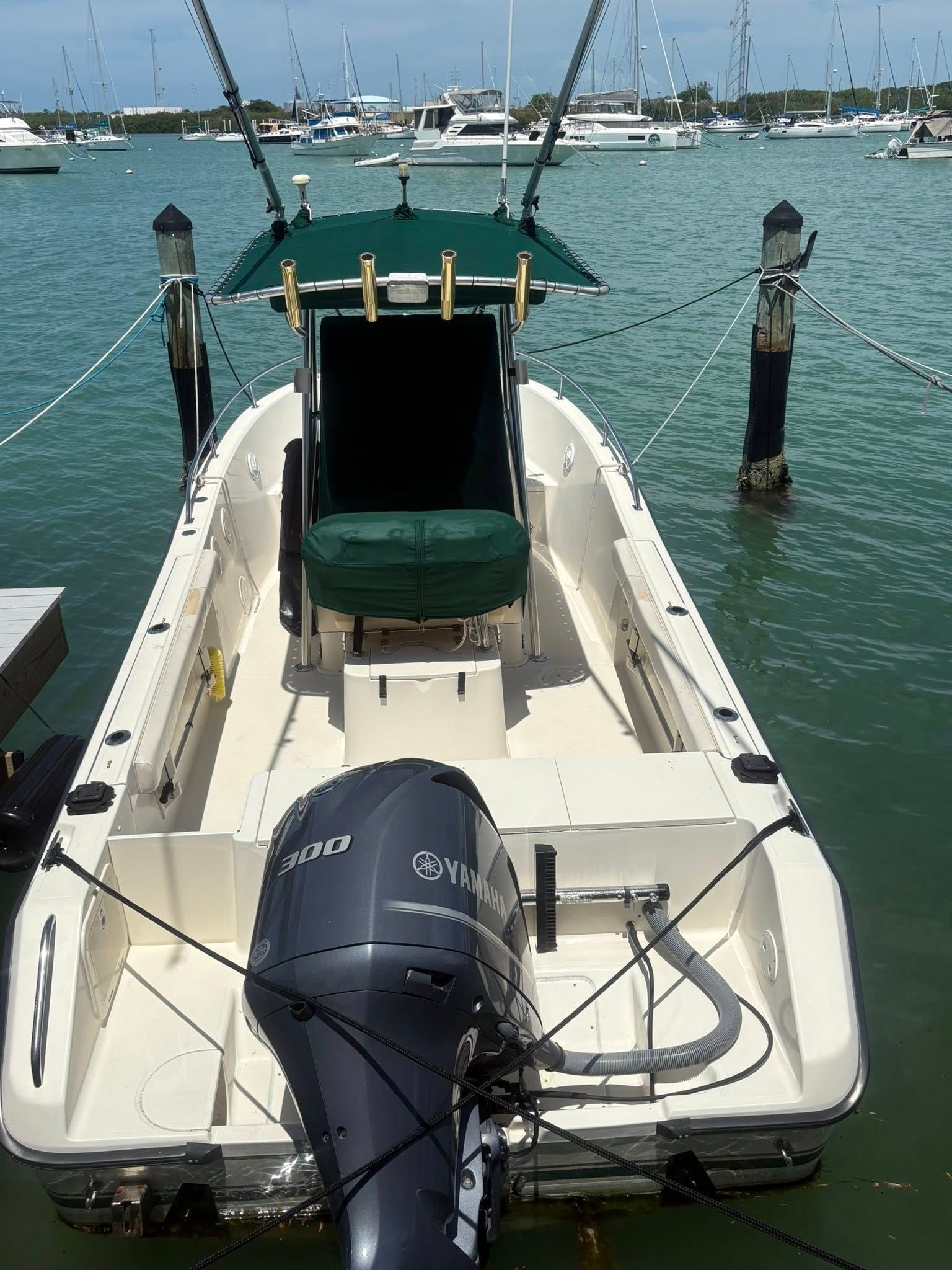 Small motorboat docked stern-first at a marina, with outboard engine and green seat under a teal canopy.