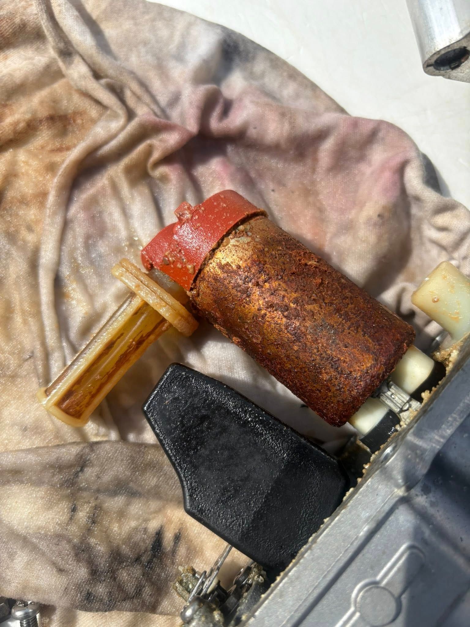 Close-up of a rusty cylindrical component with a red cap, black part, and a clear tube on fabric.