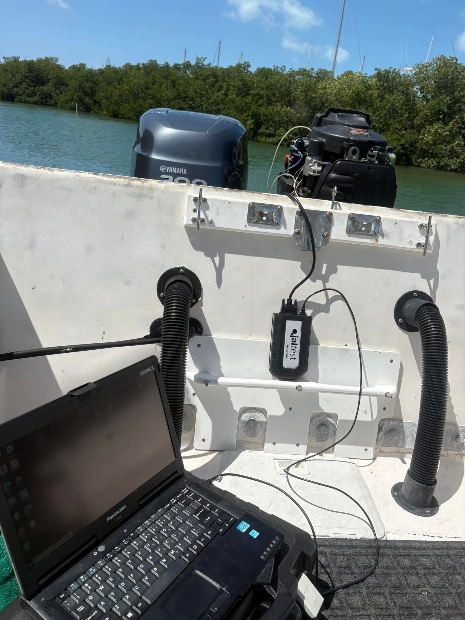 Boat cockpit with laptop, mounted equipment, and outboard motors on calm blue water near green shoreline