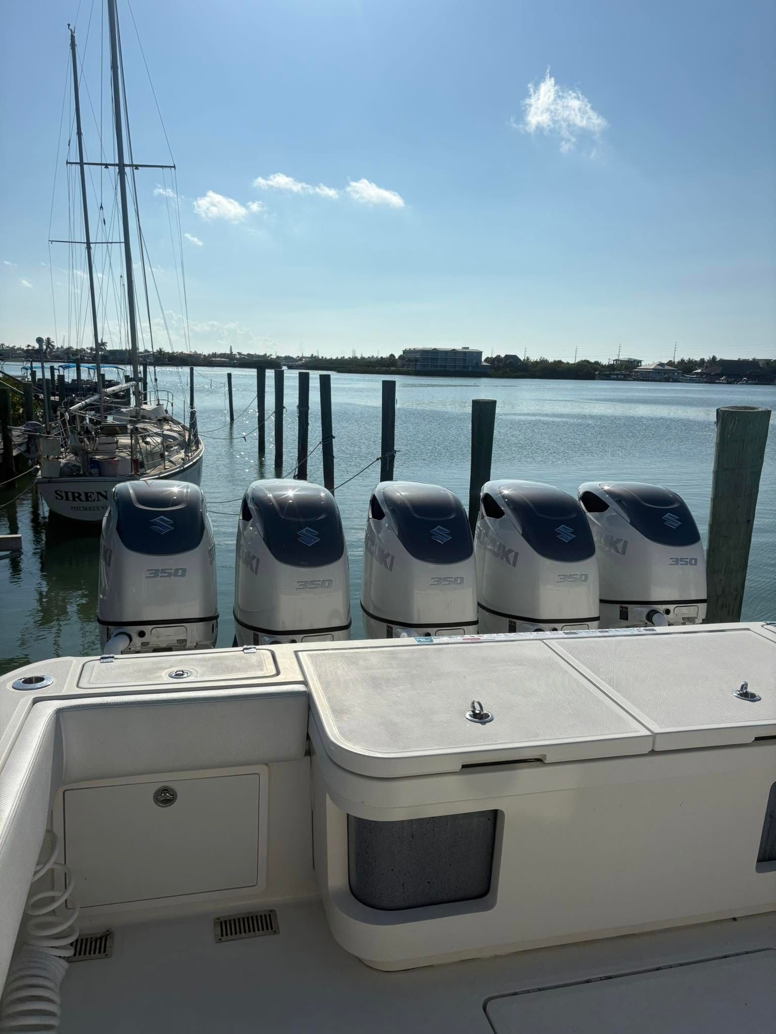 Boat stern with four outboard motors docked on calm water under a blue sky