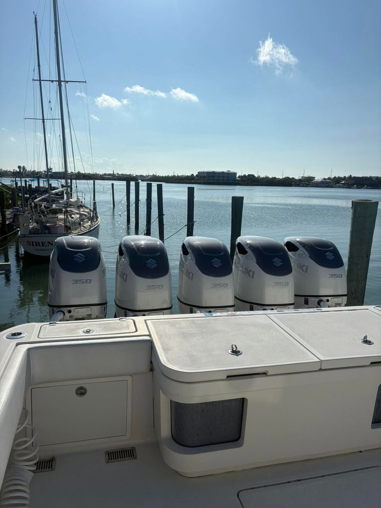 Boat stern with four outboard motors docked on calm water under a blue sky