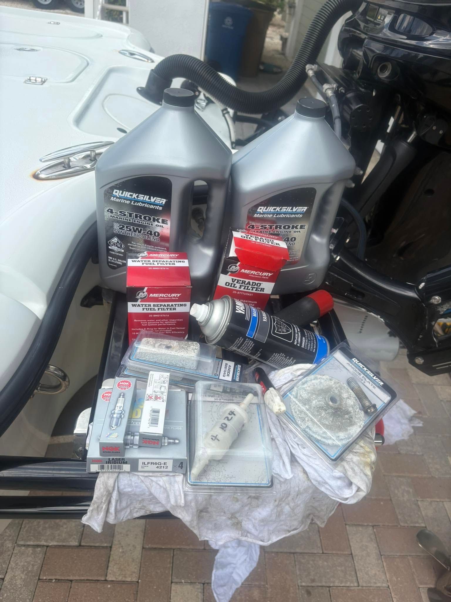 Two gray oil jugs and assorted auto parts displayed on a cloth beside parked motorcycles.