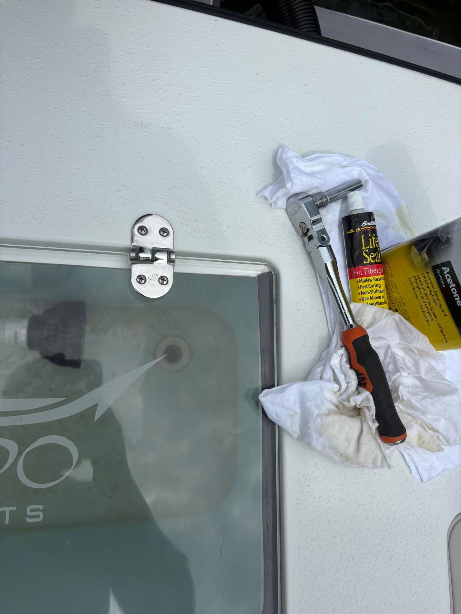 Hand tools and a yellow box on a white surface beside a glass panel hinge