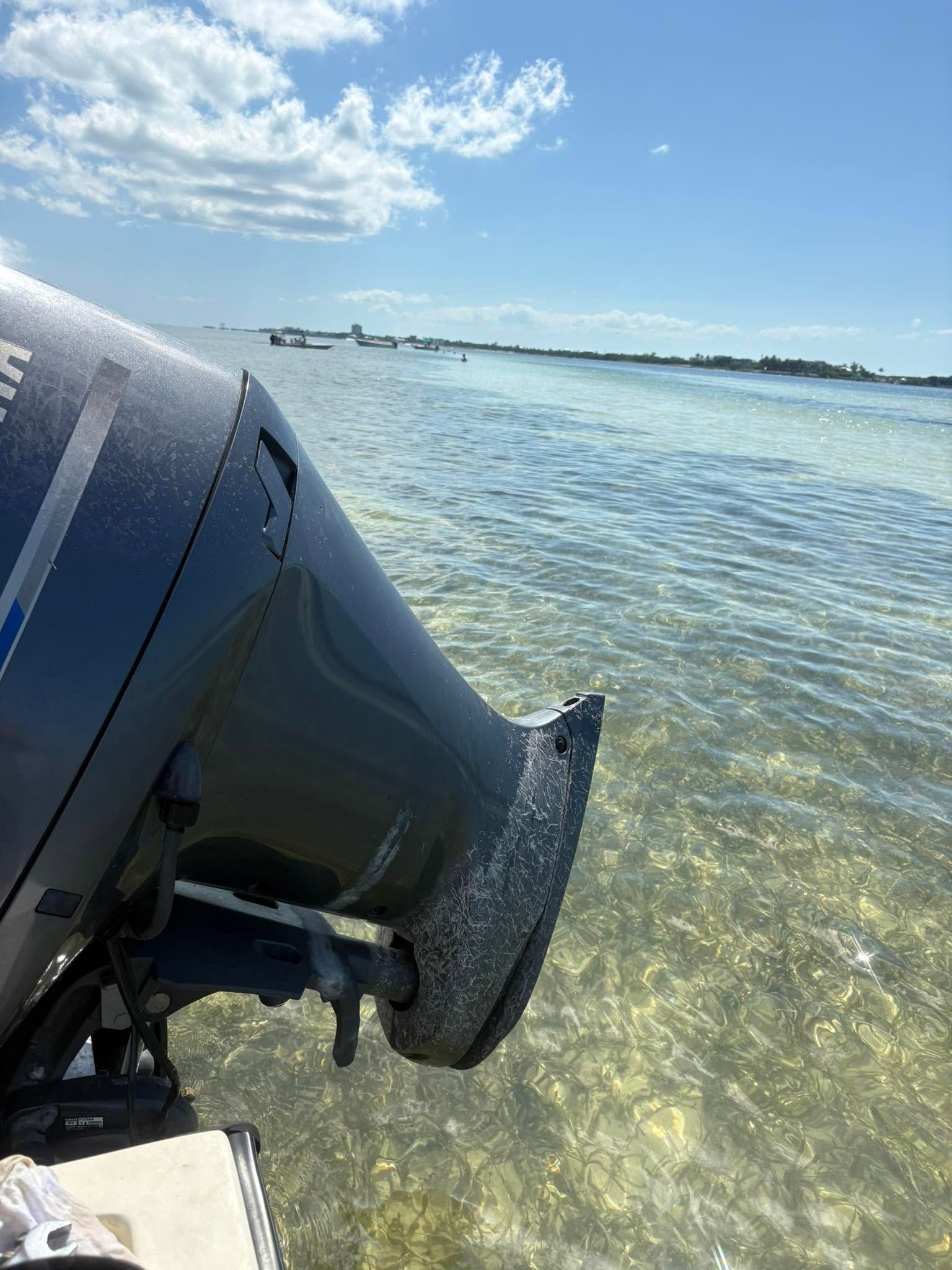 Outboard motor at the edge of clear, shallow water under a bright blue sky