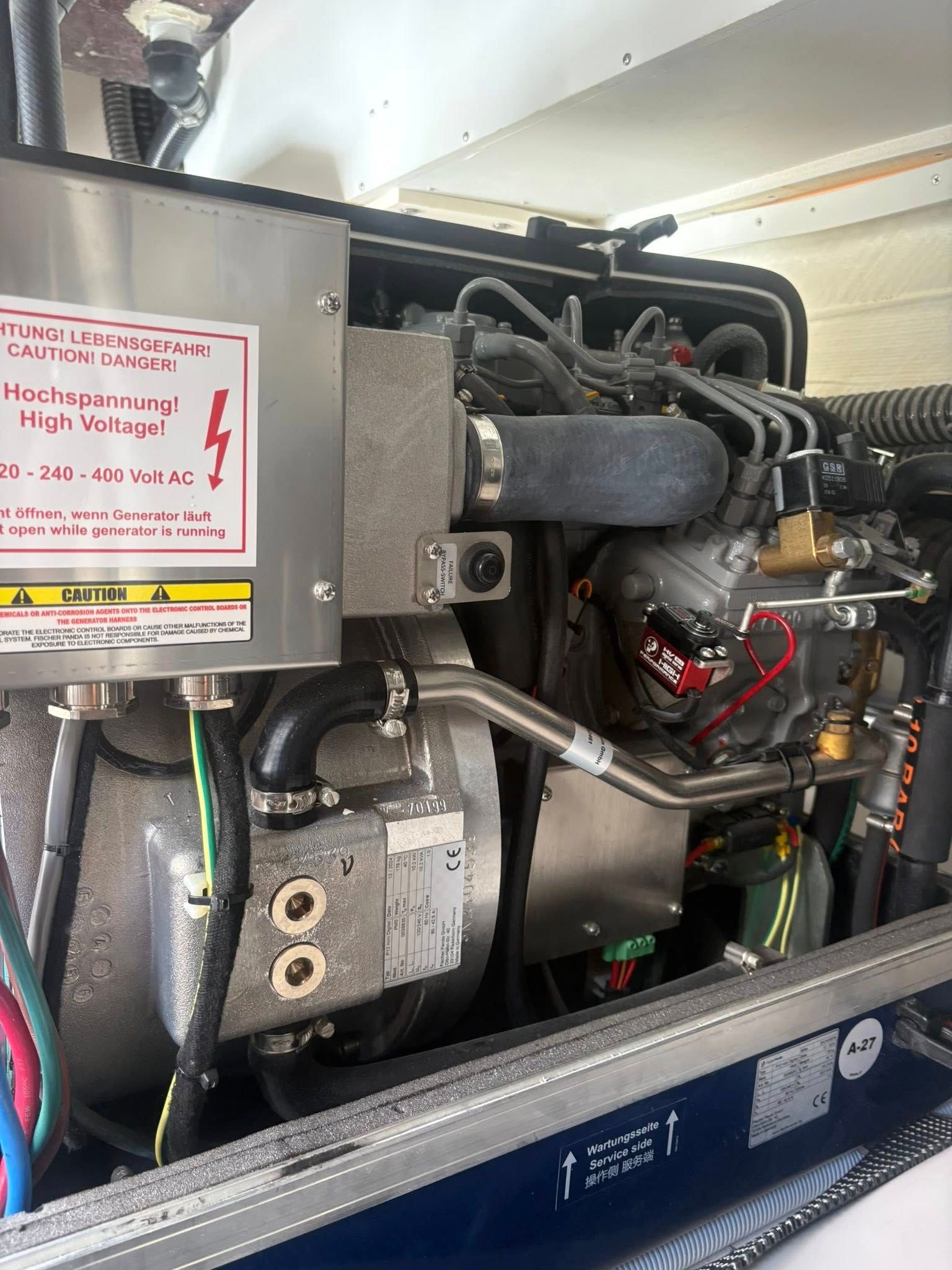Close-up of an industrial machine’s engine compartment with wiring, hoses, and a metal warning label.
