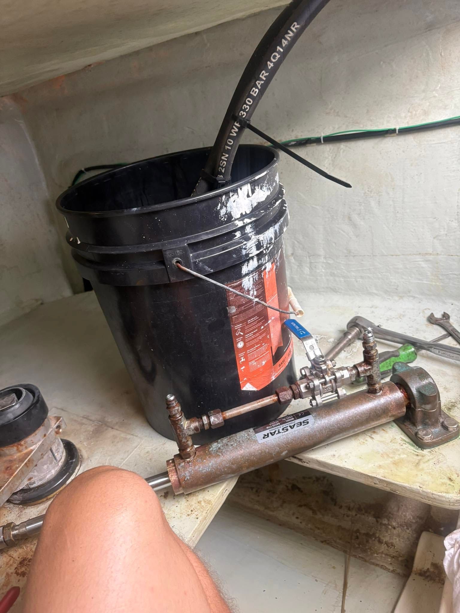 Black bucket with hose and rusty metal parts on a shelf in a cramped workspace