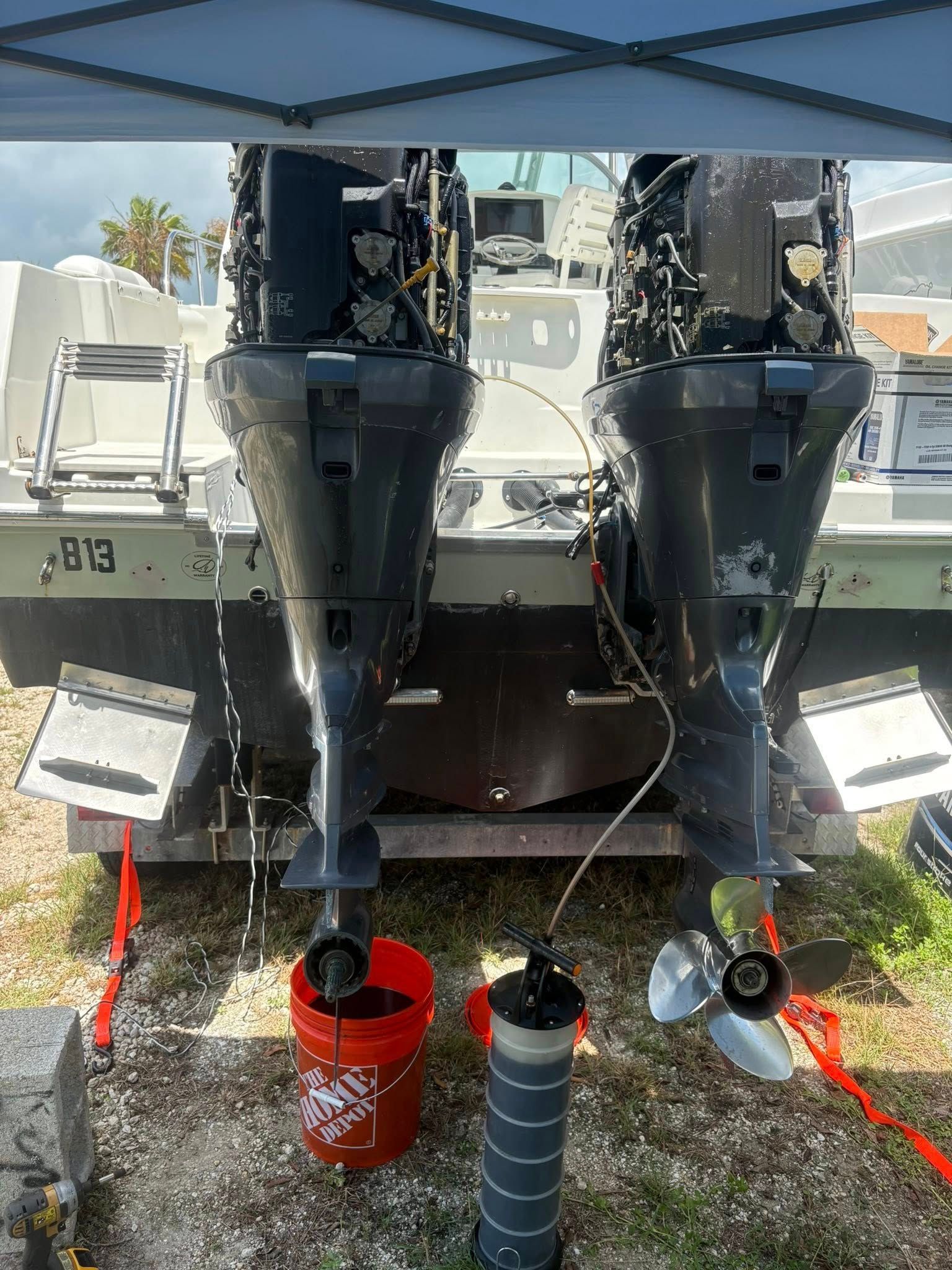 Two boat outboard motors being flushed with red buckets and hoses on a trailerable boat stern