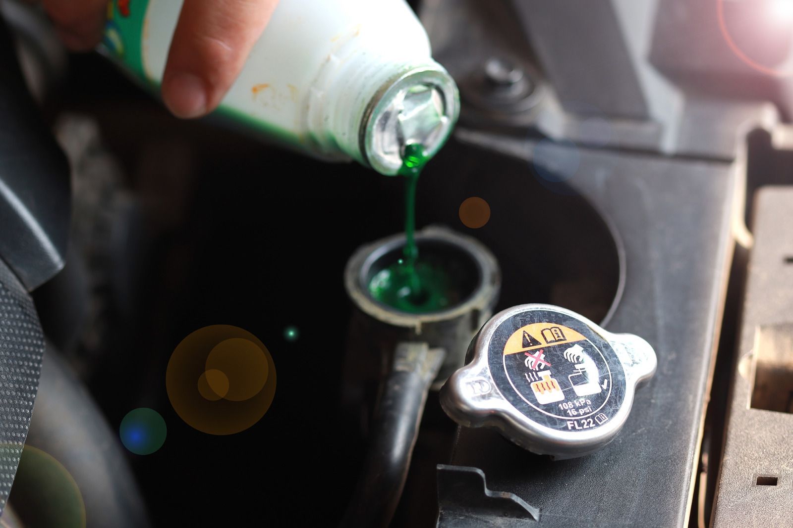 A person is pouring green coolant into a radiator cap.