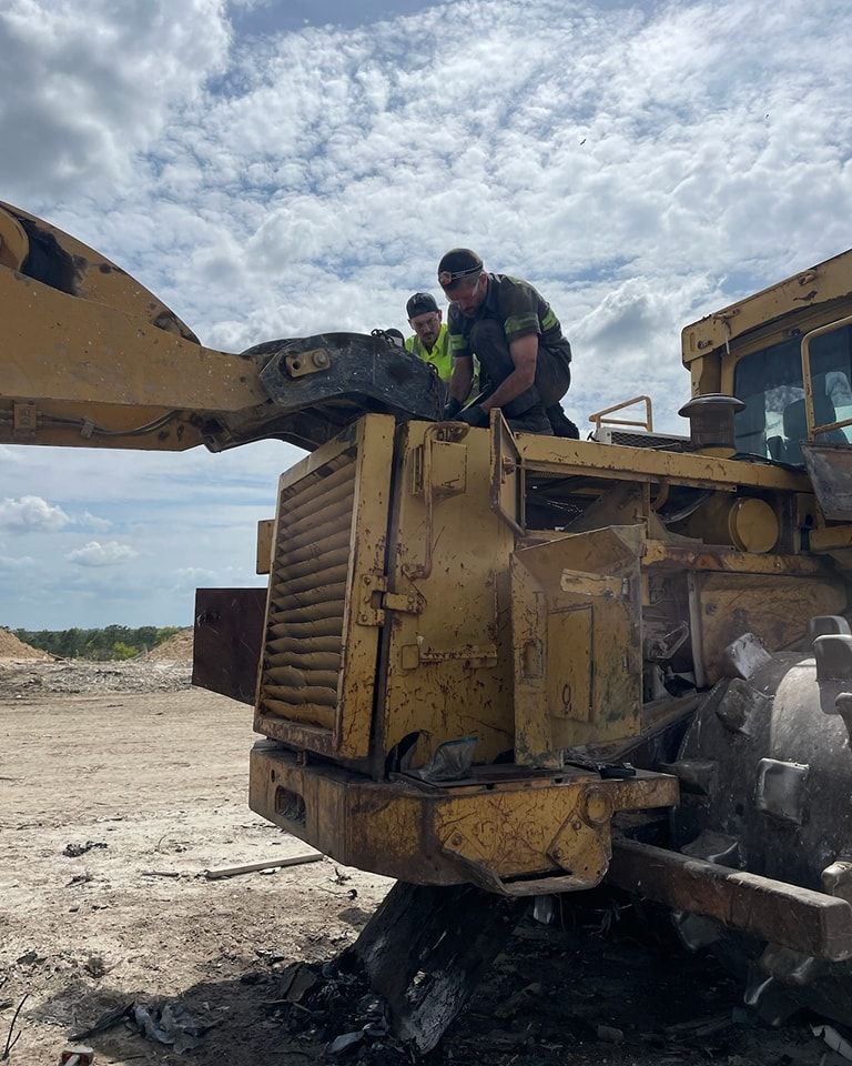 Two men are working on a bulldozer in a dirt field.