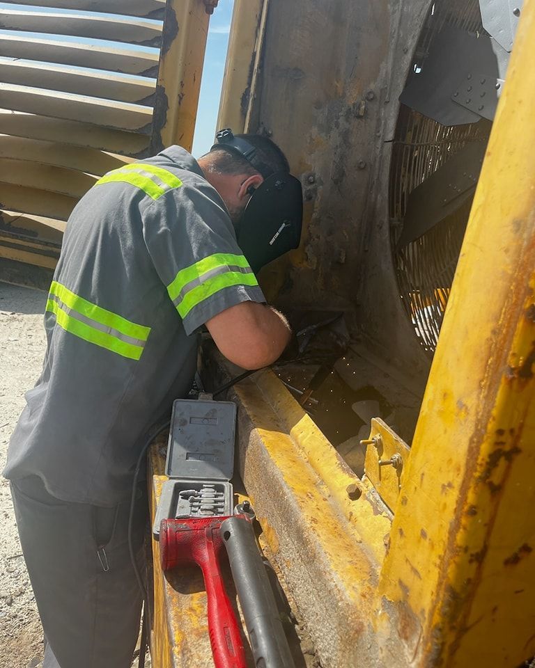 A man wearing a welding helmet is working on a machine.