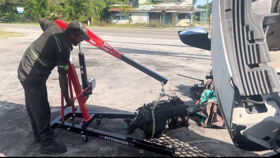 A man is working on a car engine with a crane.
